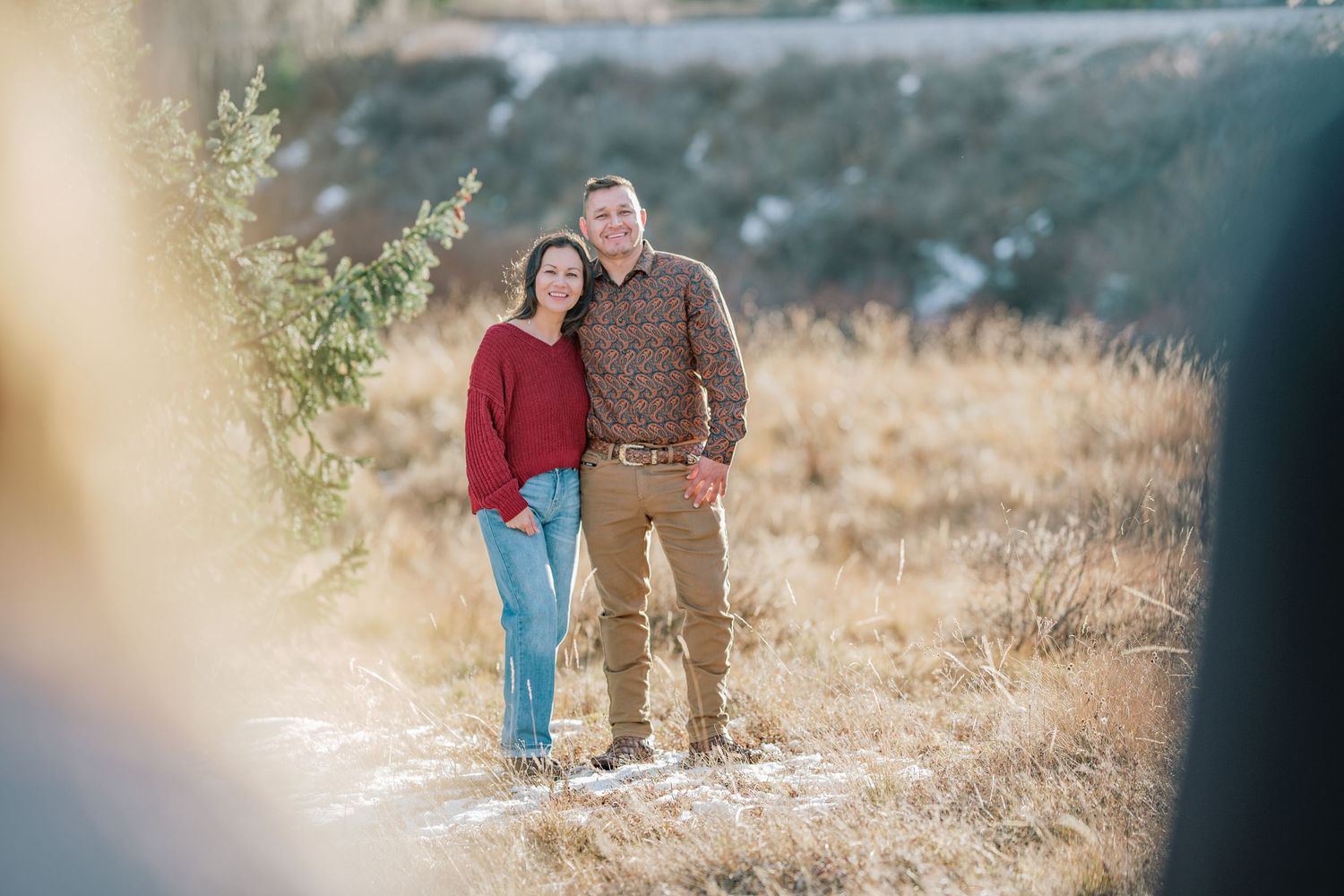 A pair walks hand-in-hand through a sunlit field with golden grass and natural lighting during autumn.