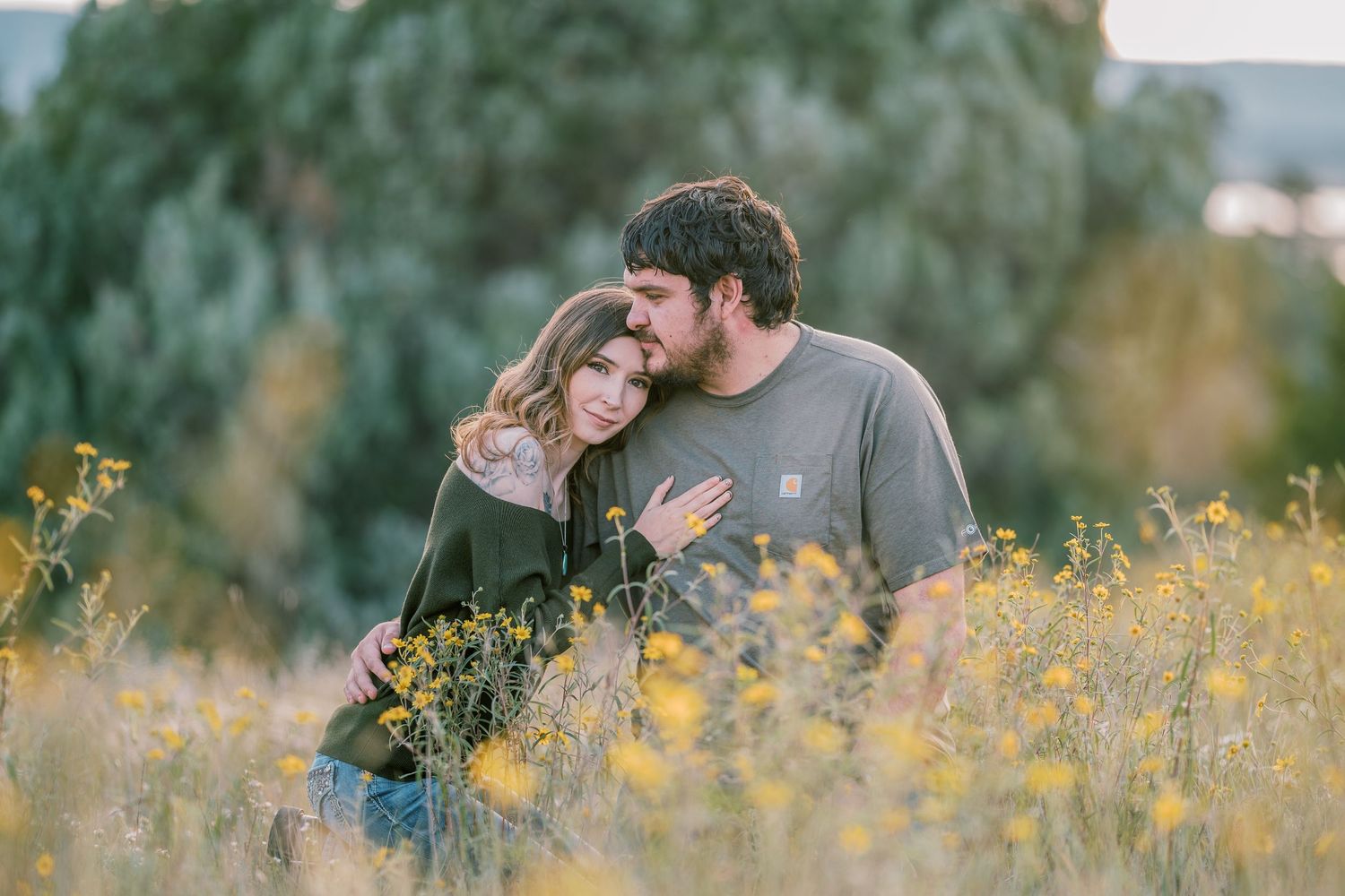 Couple embracing in a field of yellow flowers with mountains in the background.