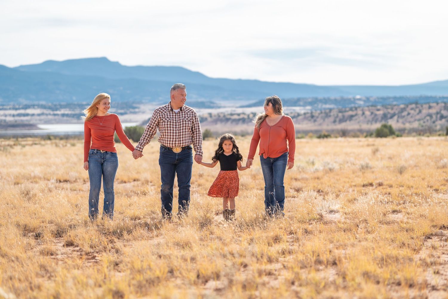 Family of four walking through brown grass in Abiquiú's desert landscape — warm, natural light photo by Quiet Light by The Amoras.