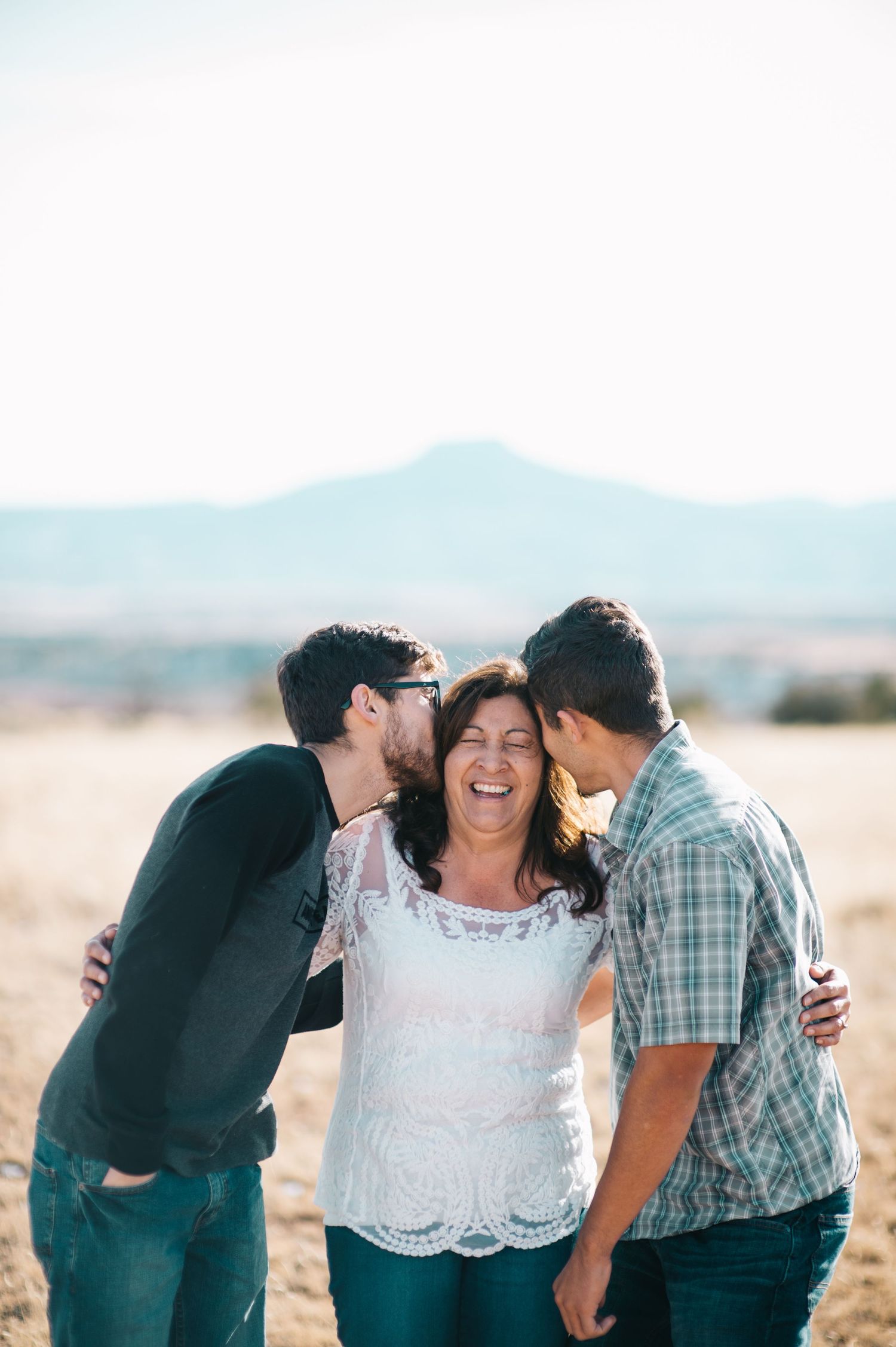 Candid shot of mother and two adult sons embracing in the open desert of Abiquiú — heartfelt storytelling by Quiet Light by The Amoras.