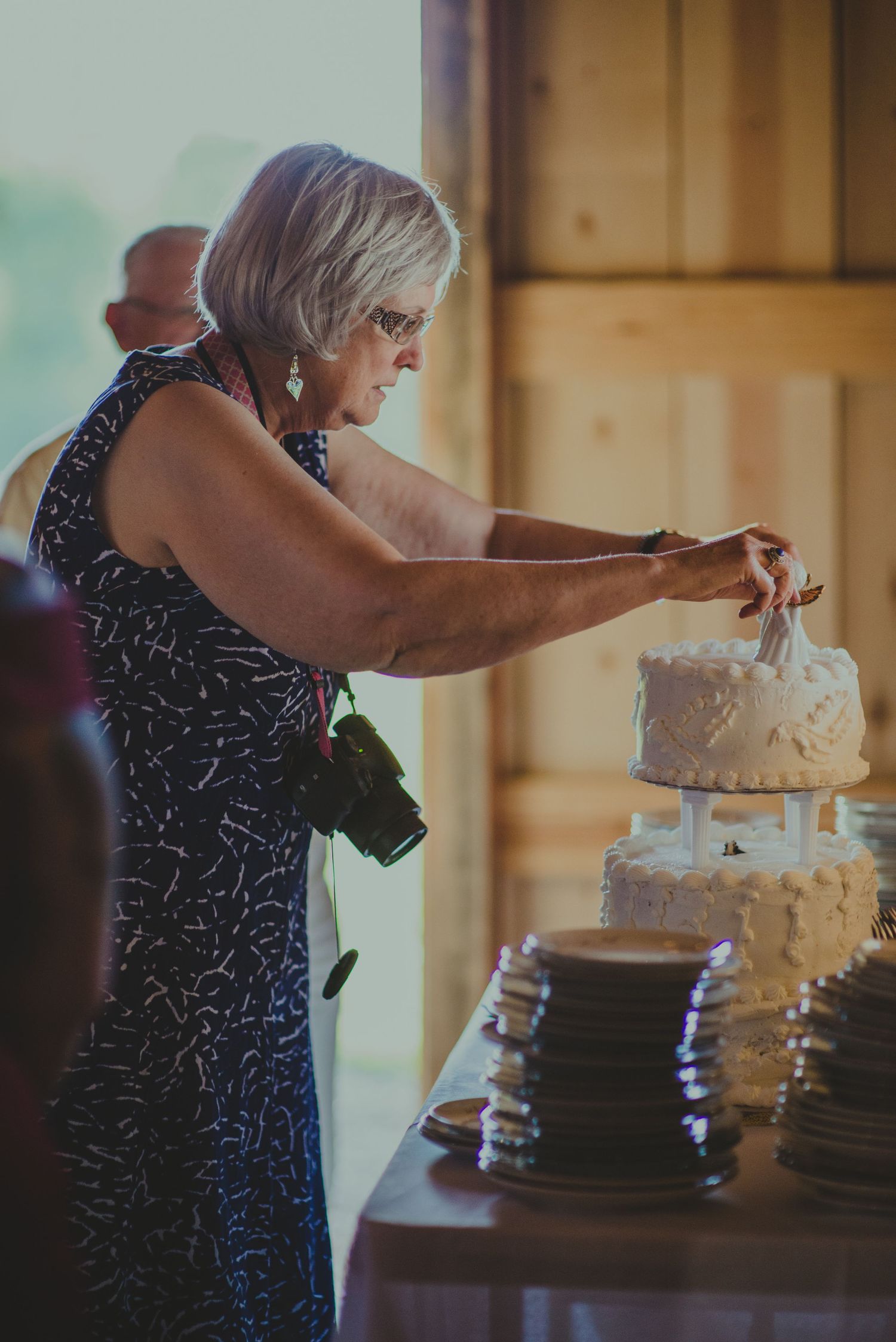 Woman cutting an elegant white tiered wedding cake at a rustic barn reception.