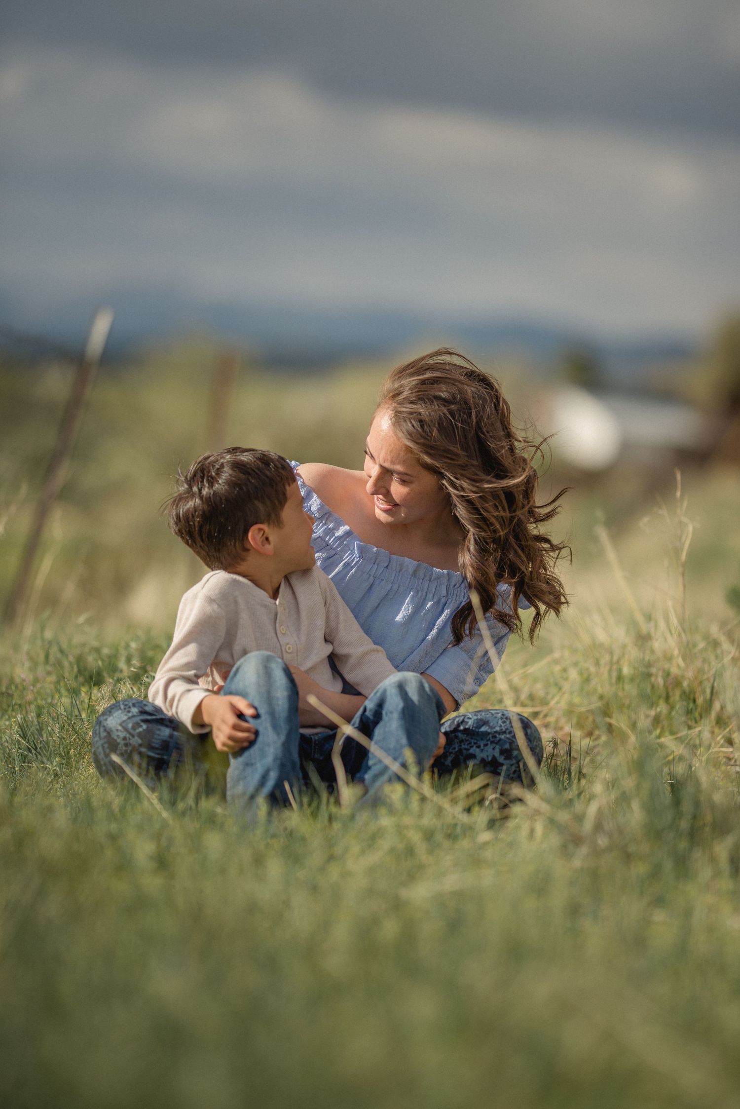 A parent and child lie together in tall grass on a sunny day enjoying precious family time outdoors.