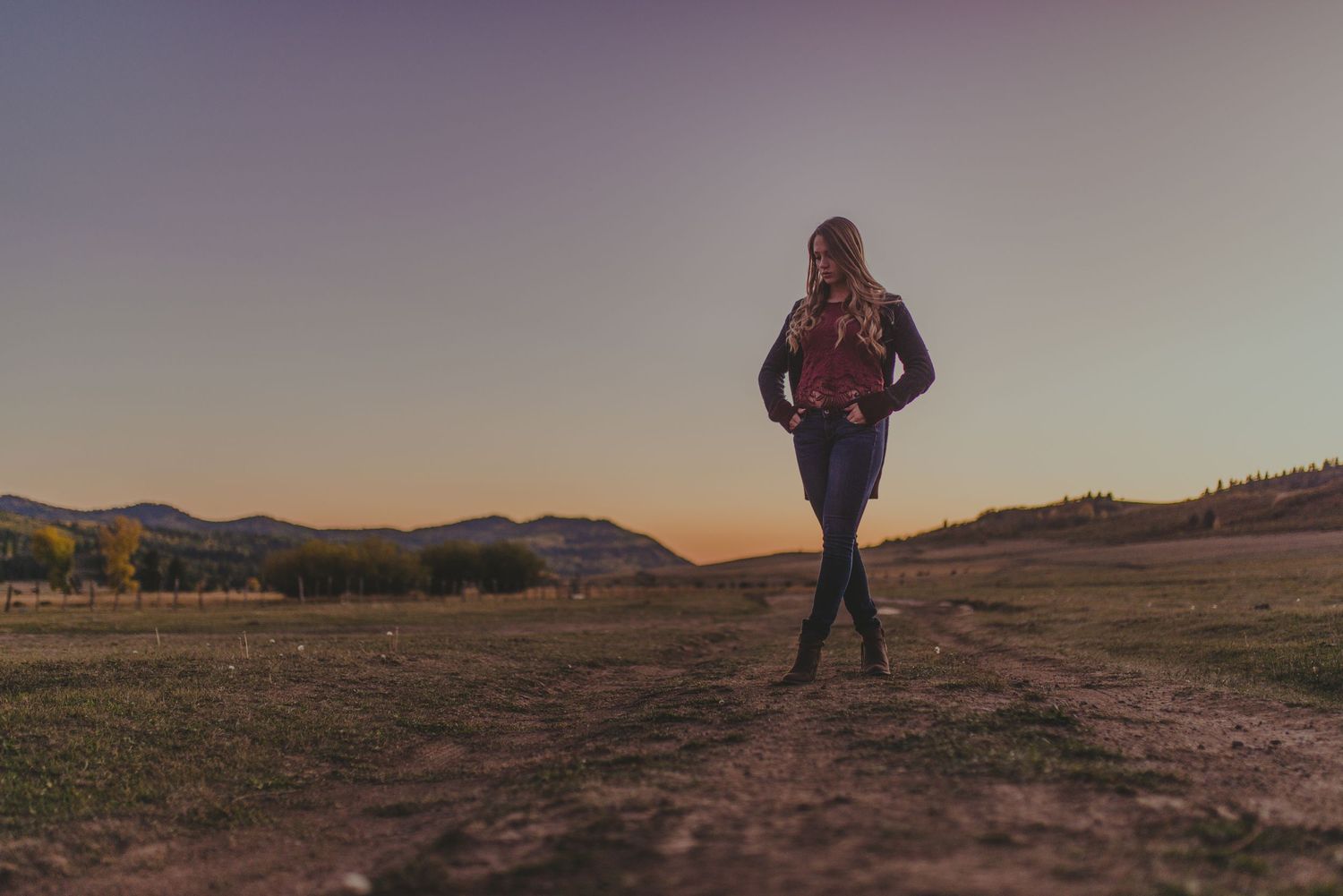 Person standing on hill at dusk with dramatic golden light and mountains in background.