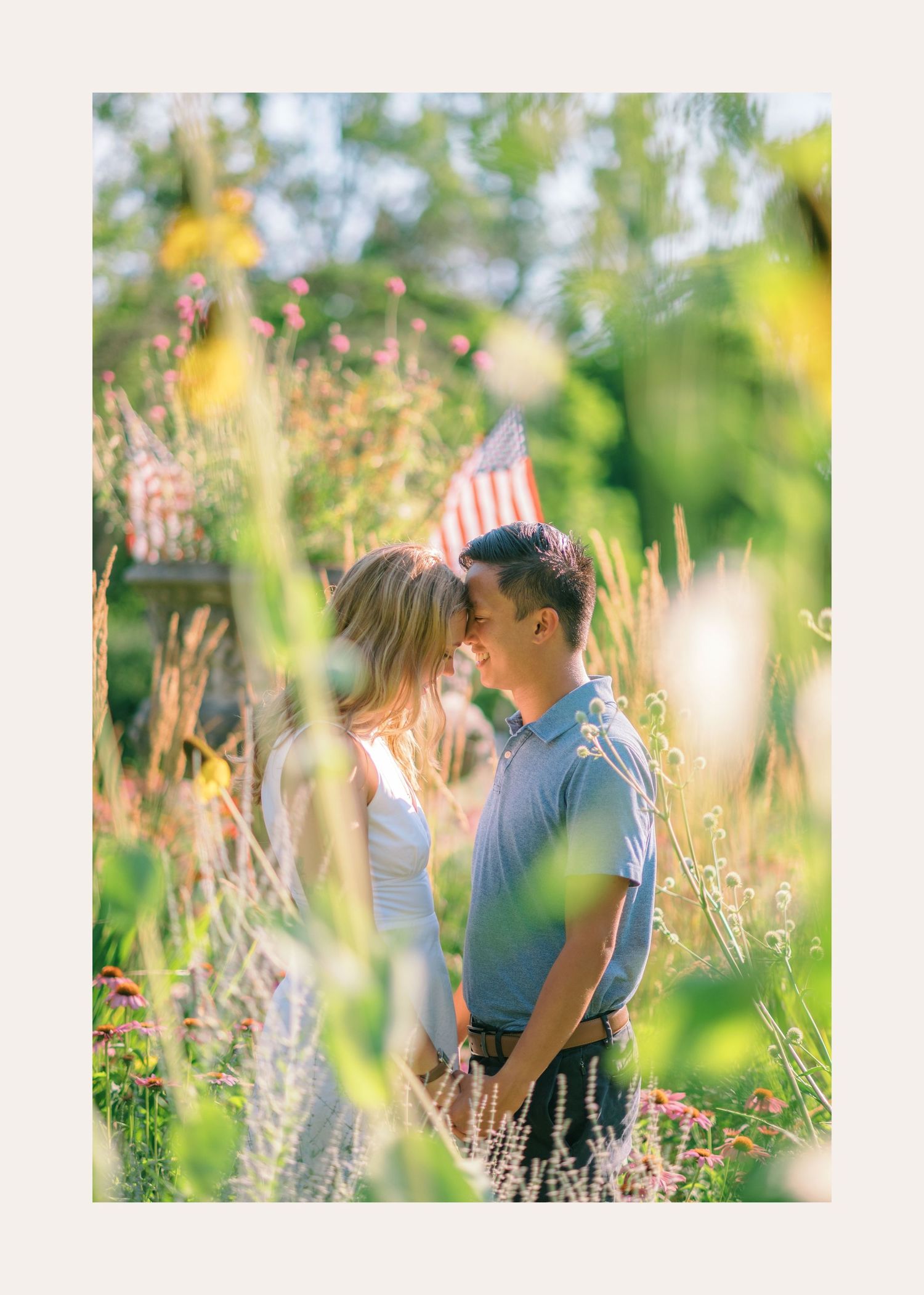 A couple shares a romantic moment while standing in a meadow of tall grass and wildflowers on a sunny day.