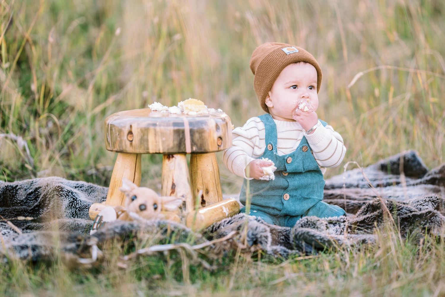 Figure wearing green overalls resting on a log surrounded by autumn grass and wooden decor.