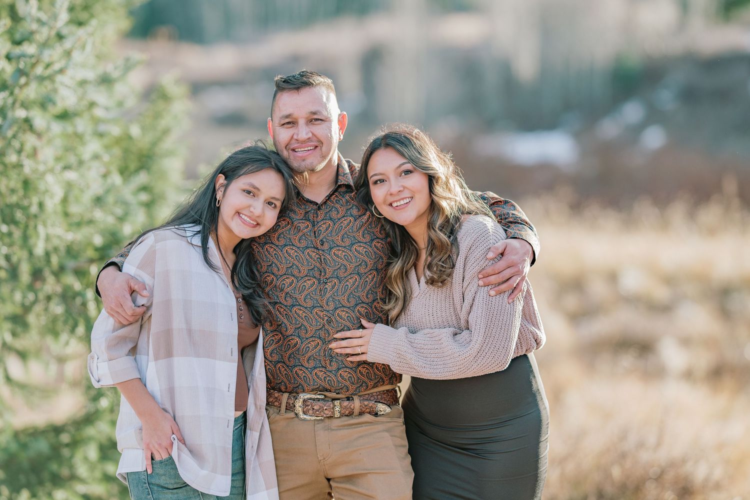 A group poses together in an outdoor setting with natural brown grass and greenery in the background.