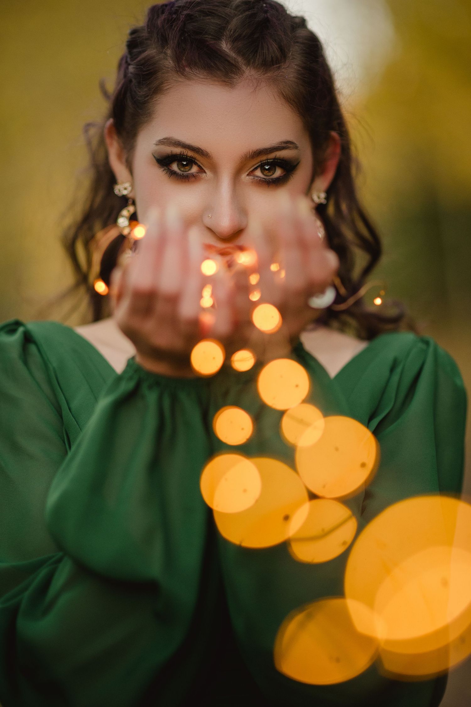 A close-up portrait with glowing golden bokeh lights and a green sweater creating a dreamy holiday atmosphere.