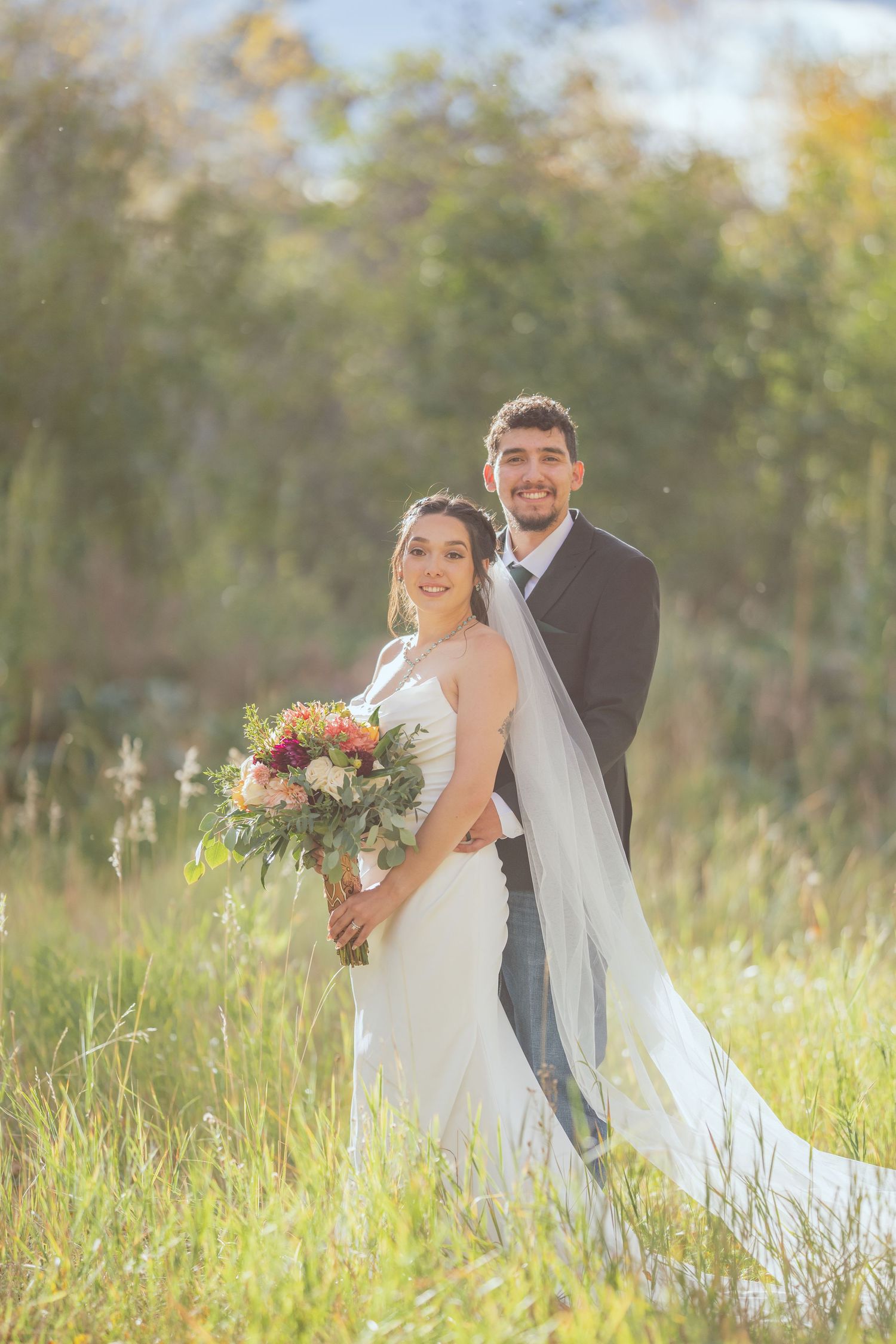Wedding portrait in a golden autumn field with flowing white dress and colorful bouquet.