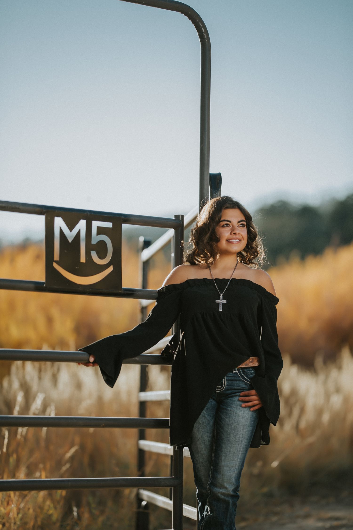 Casual portrait against rustic metal gate with golden field in background.