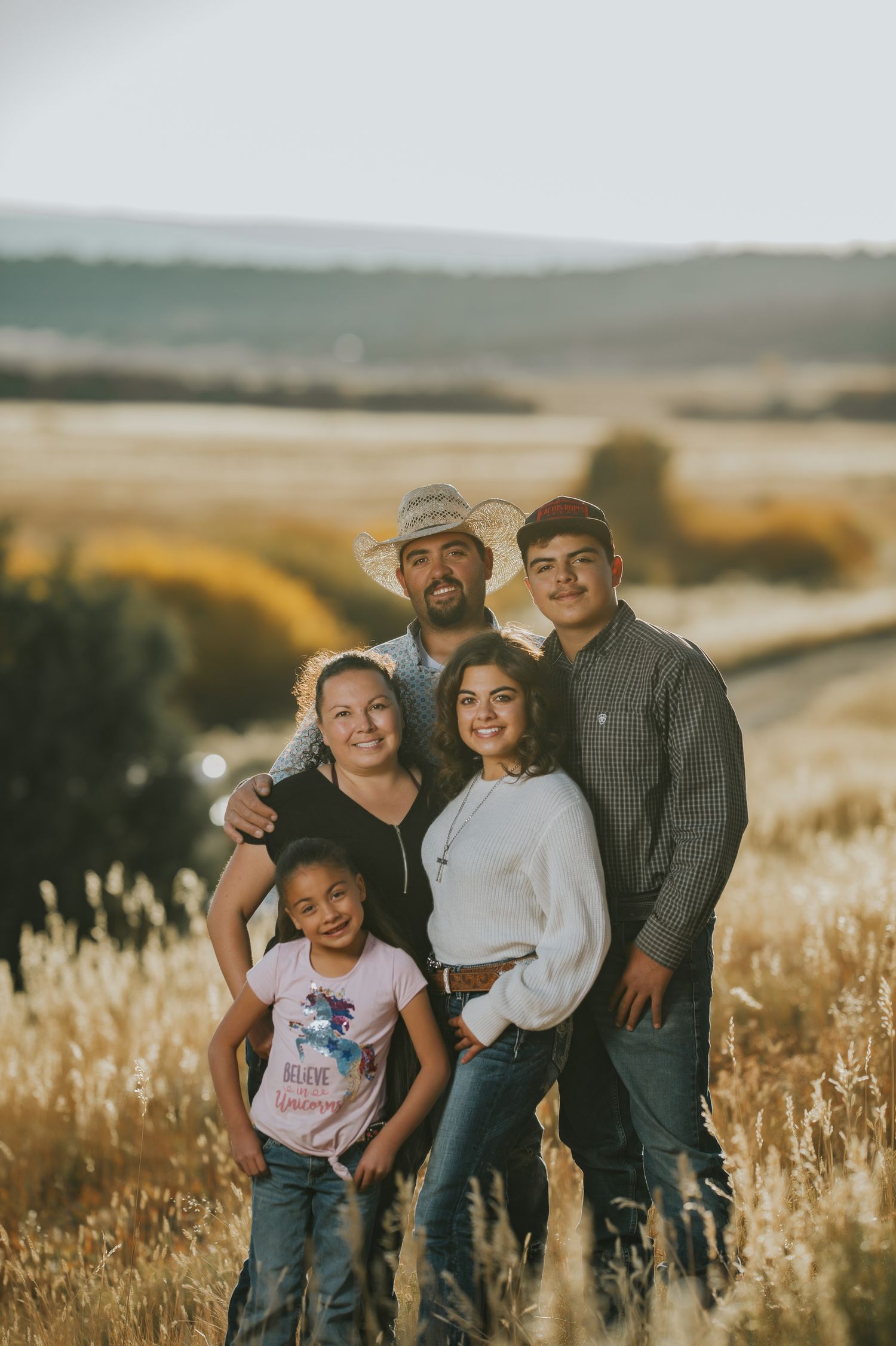 Family portrait in wheat field with rolling hills in background during sunset.