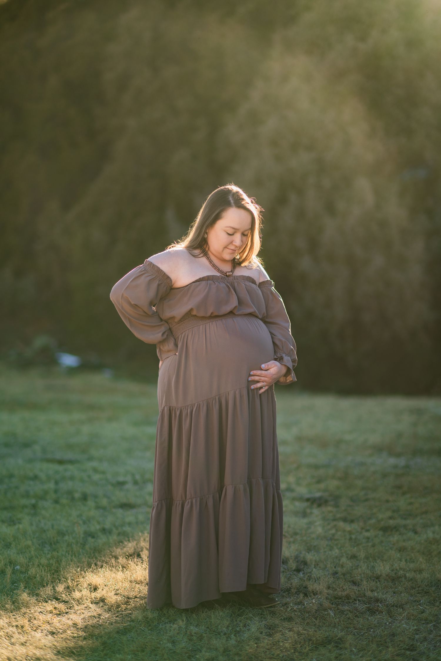 A person in a flowing mauve dress poses gracefully in a sunlit field during golden hour.