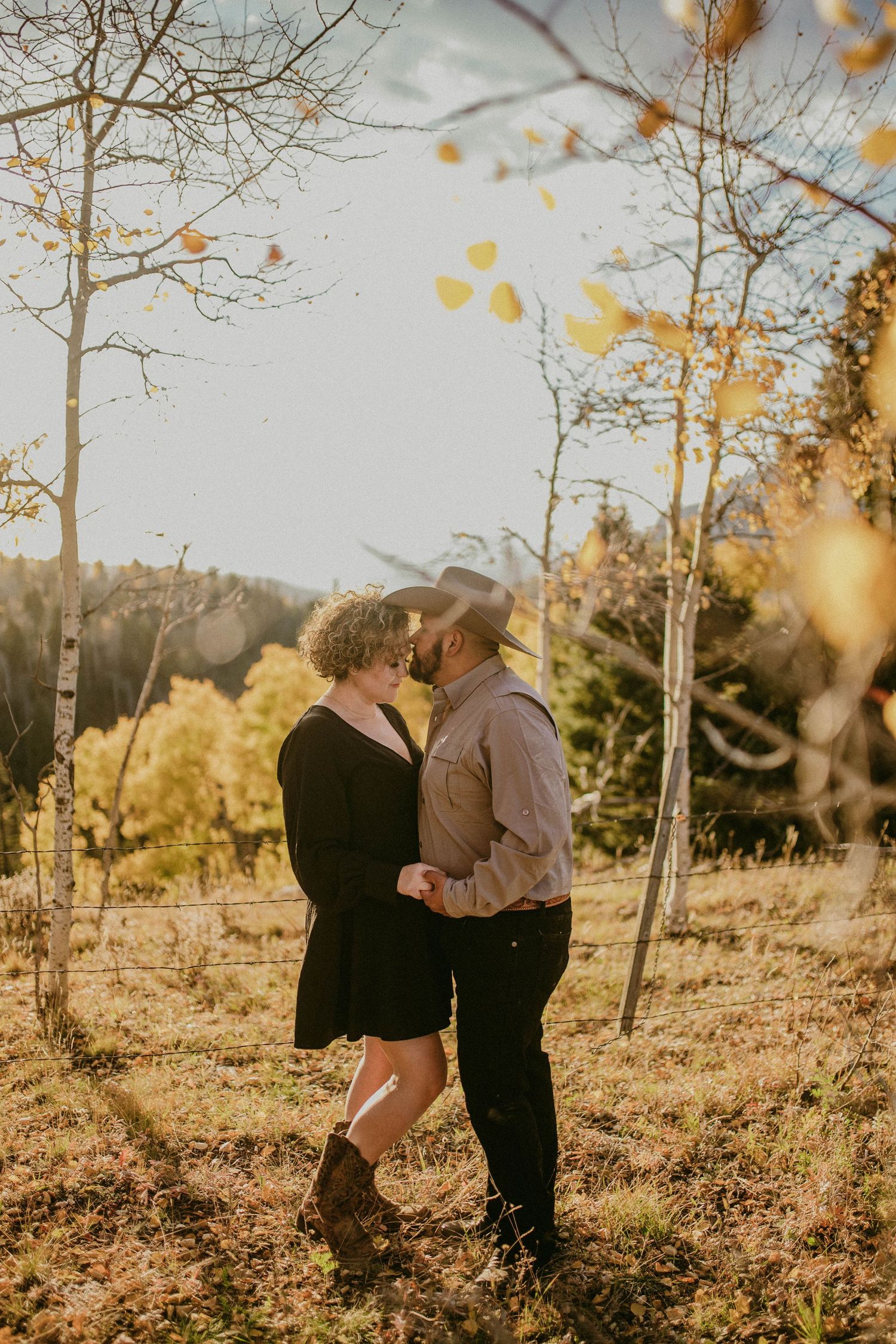 A couple embraces in an aspen grove with golden fall foliage and warm sunlight filtering through.