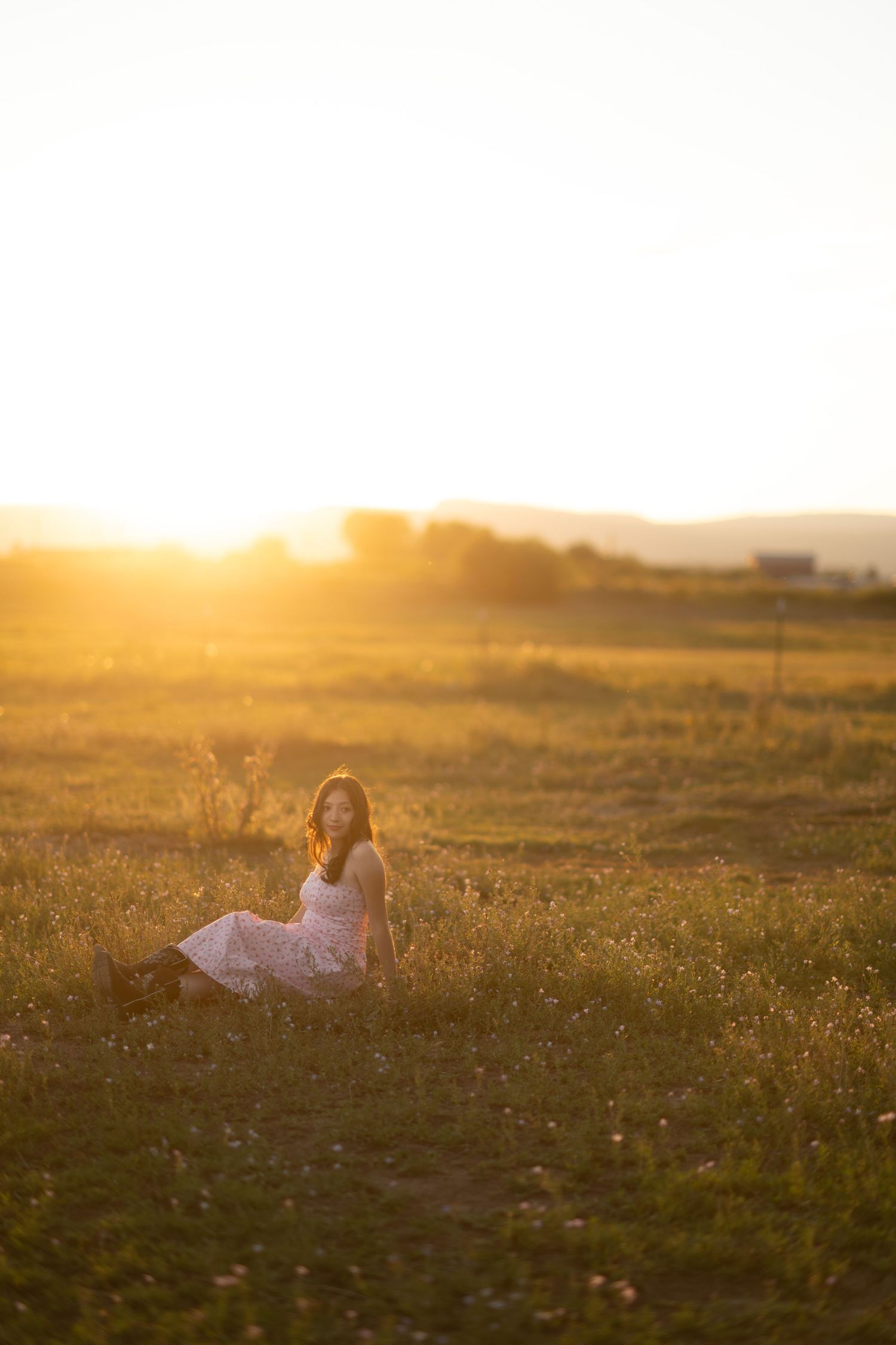 Dreamy scene of someone in a white dress lying in a golden wildflower meadow at sunset.