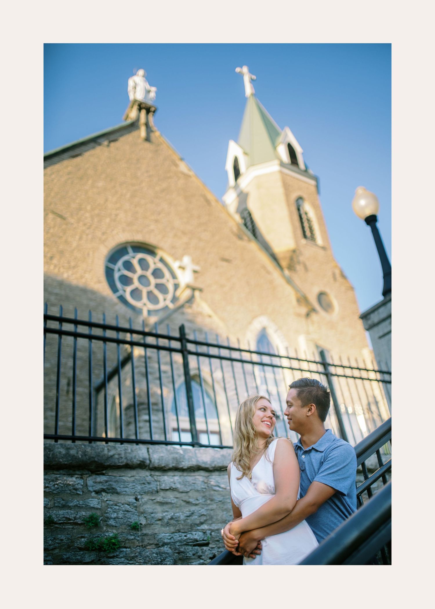 A couple shares an intimate moment outside a stone church with gothic architecture details in warm afternoon light.