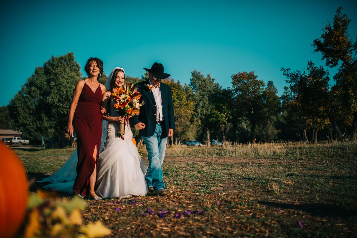 Autumn wedding party posing outdoors in golden sunlight with pumpkins and fall foliage.