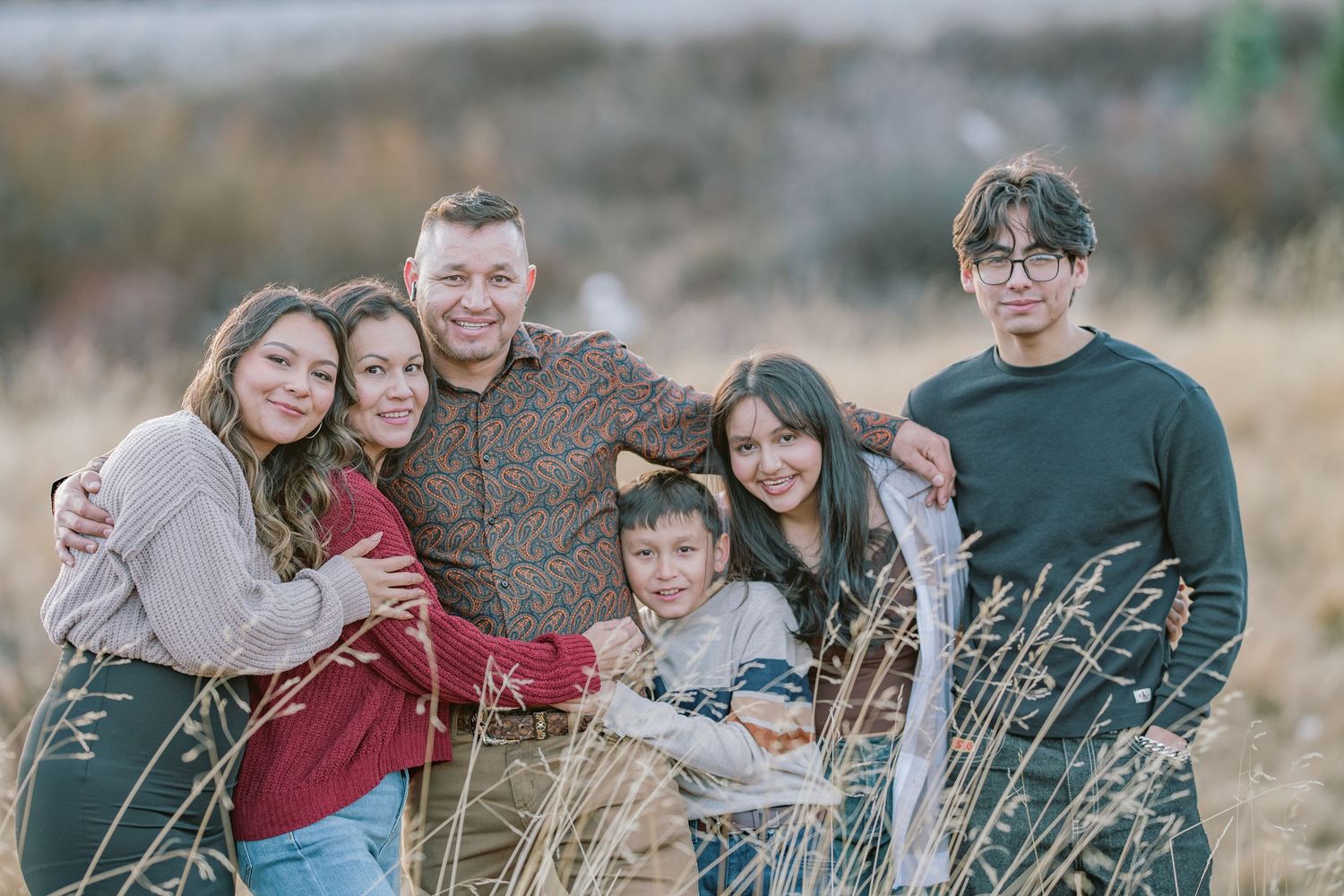 A group of people smiling together while standing in a field of tall grass during golden hour.