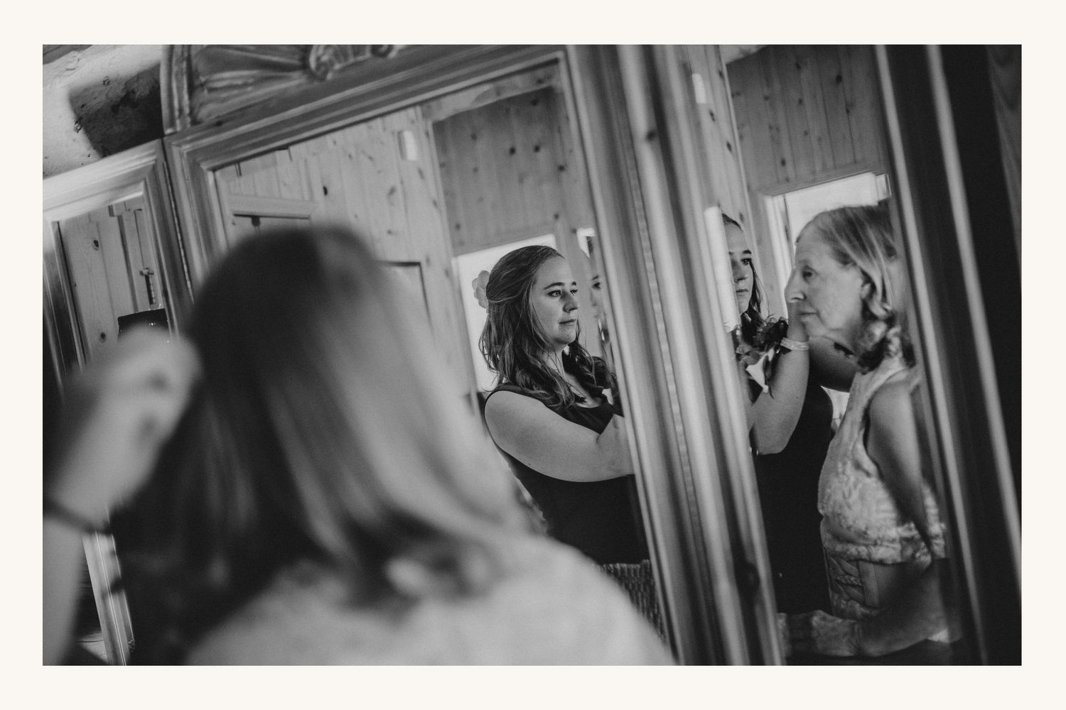 Black and white photo of women getting ready, reflected in a large mirror during bridal preparations.