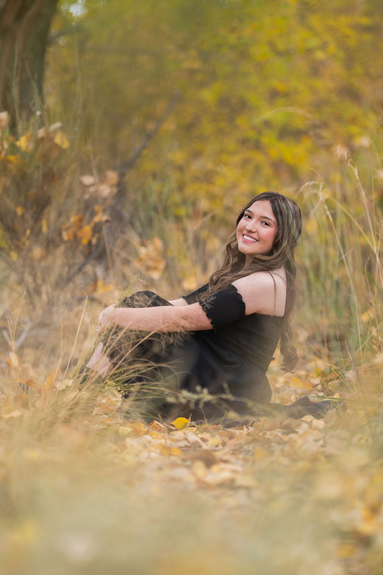 Portrait of someone relaxing outdoors in autumn setting with yellow foliage background while wearing a black dress.