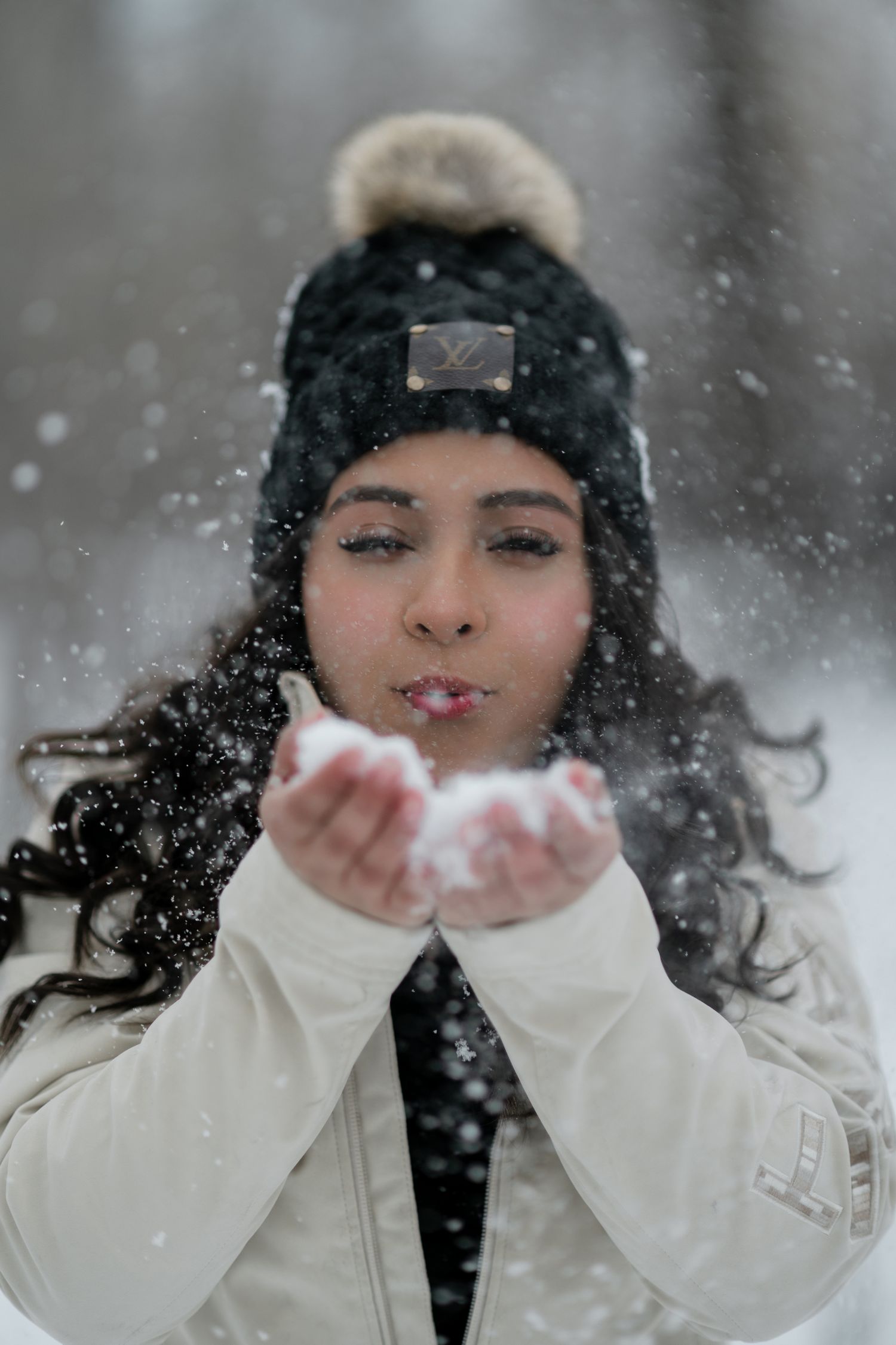 A person wearing white gloves and a dark hat blows snow from their hands in a magical winter scene.
