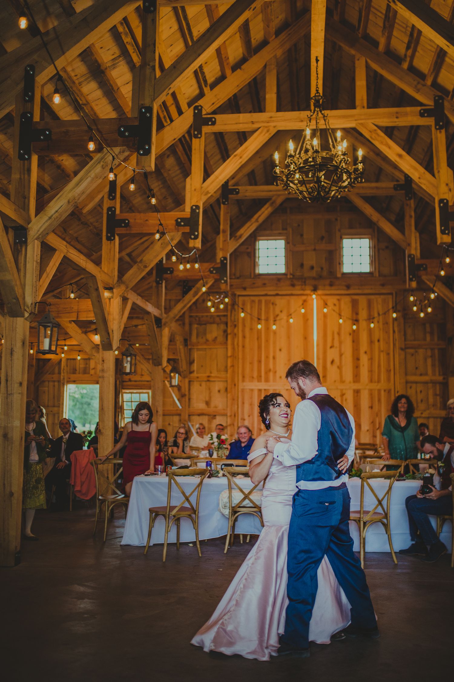 First dance in rustic barn venue with wooden beams and hanging lights.