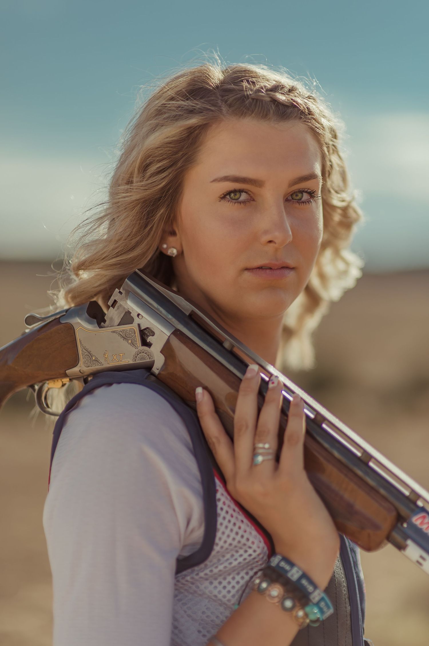 Person holding shotgun in desert setting with soft lighting and cloudy sky.