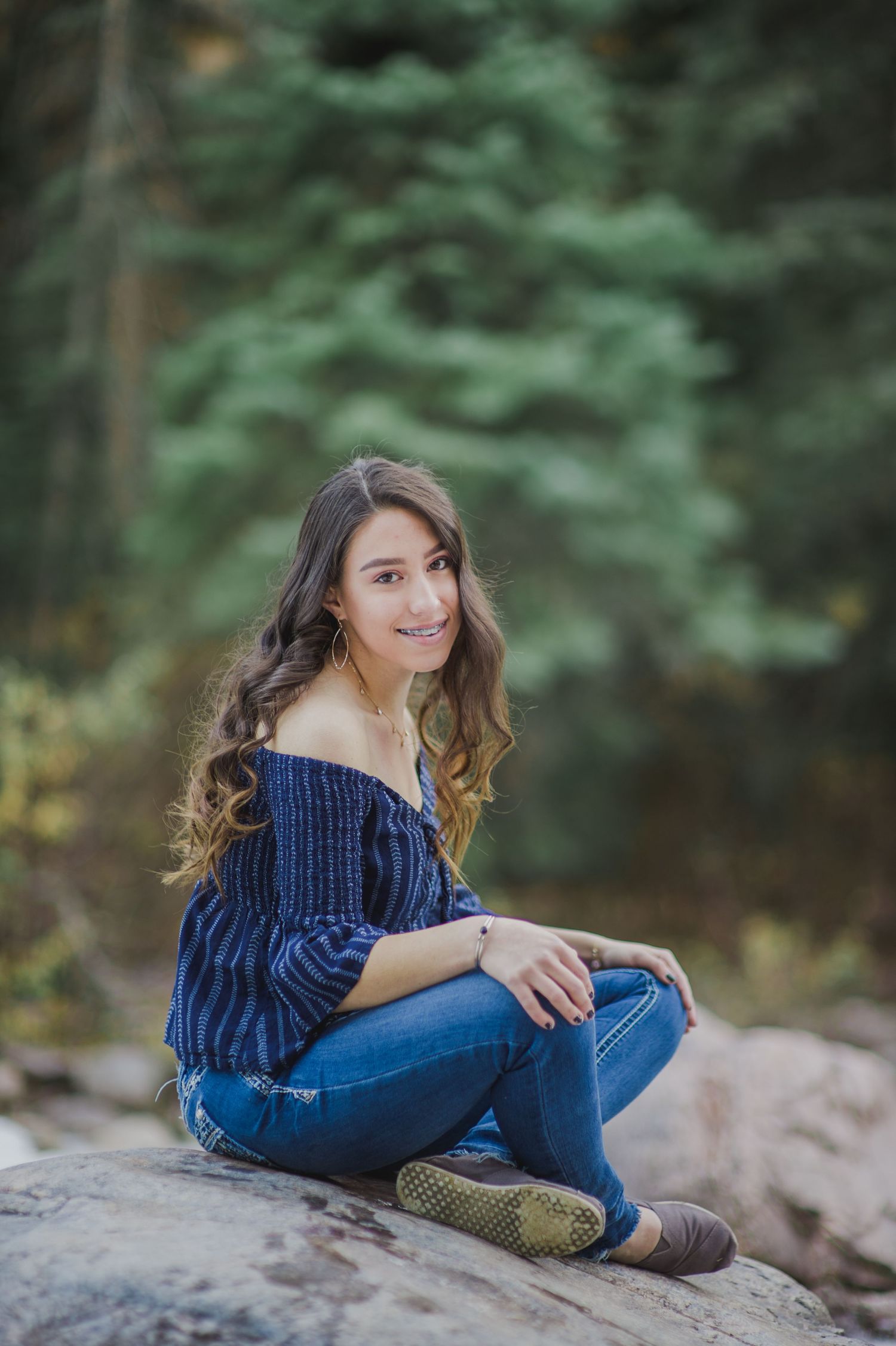 Casual portrait on rocky terrain wearing blue sweater and jeans in mountain setting.