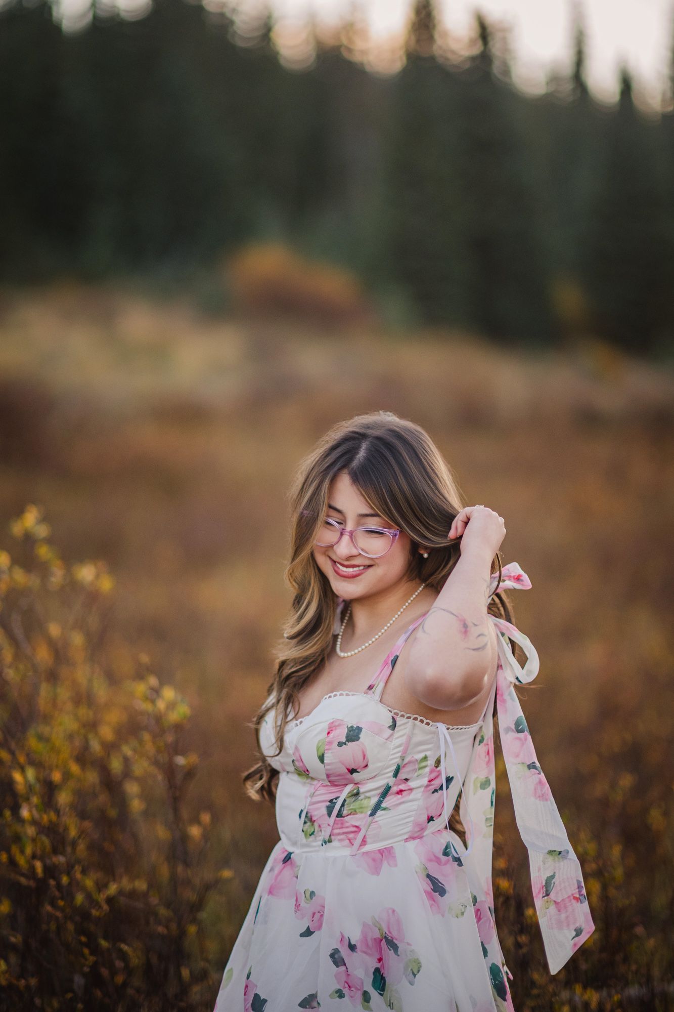 Woman in a floral dress and glasses smiling in an autumn field with evergreens near Chama, New Mexico.