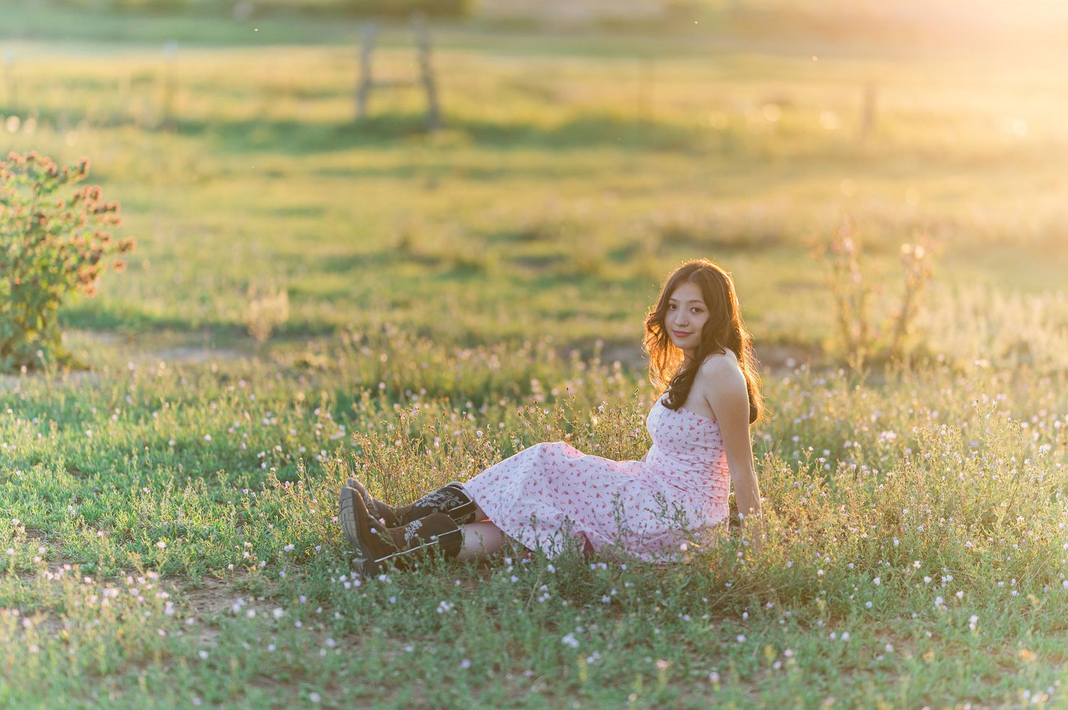 A person lies on a green meadow at sunset while a small dog sits nearby in warm golden light.