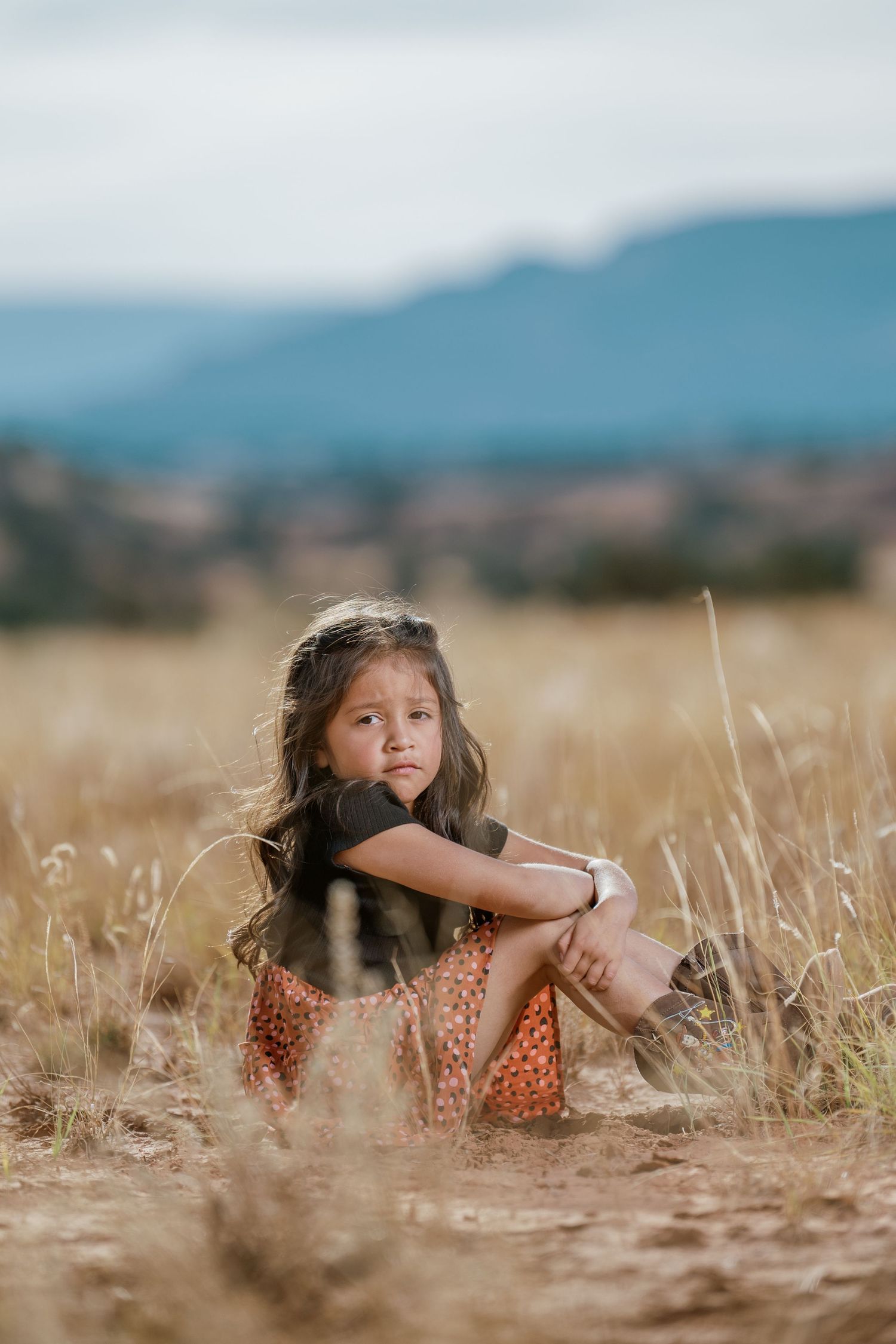 A joyful scene in a golden wheat field shows someone wearing a polka dot dress lying among the tall grass.