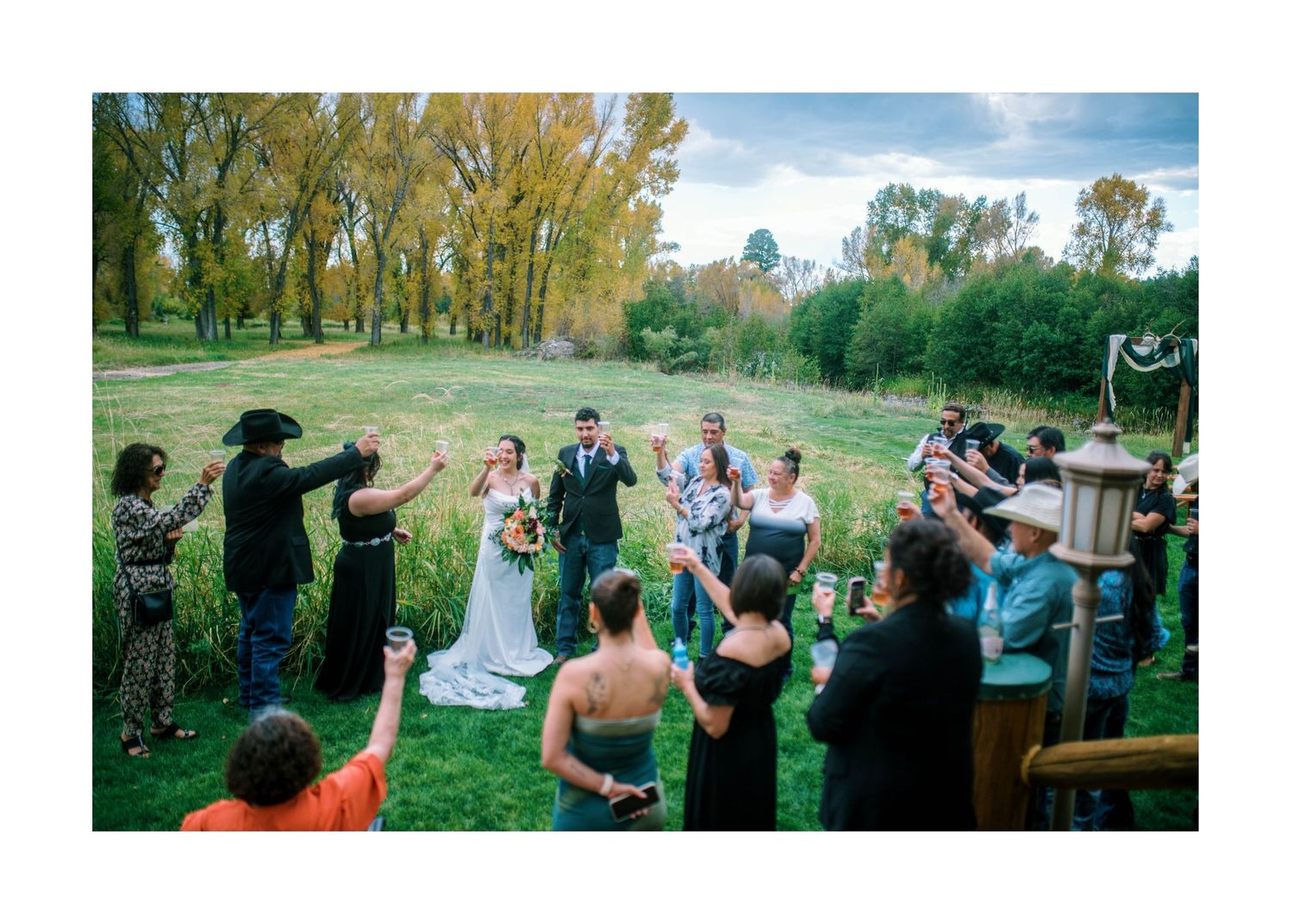 Outdoor wedding guests photograph ceremony and celebrations on mobile phones in a natural setting.