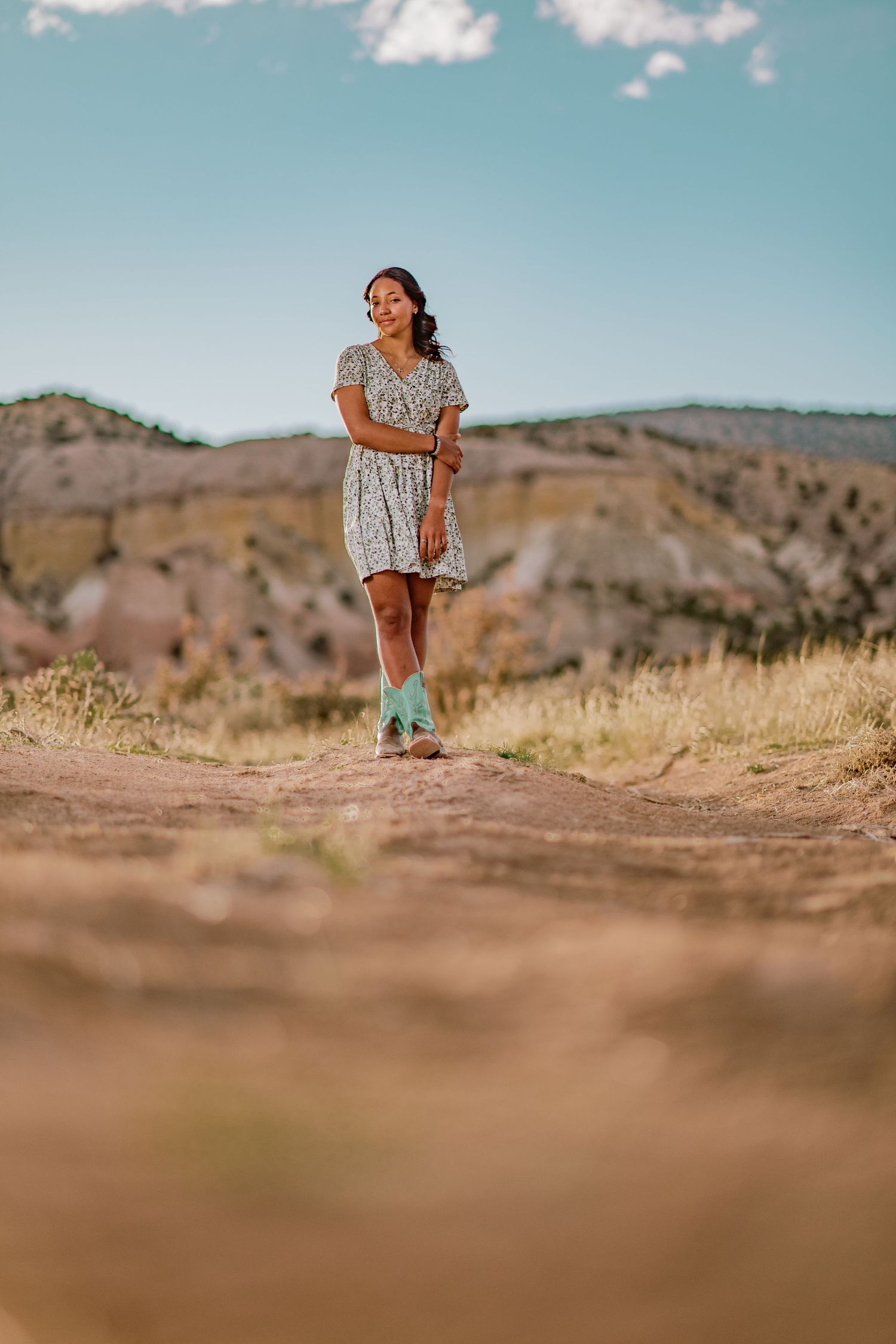 Senior girl standing in golden grass with teal-blue skies in Abiquiú — spring portrait captured by Quiet Light by The Amoras.