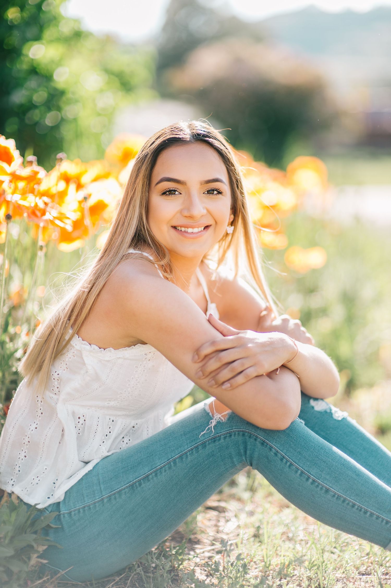 Portrait of a senior girl seated in a grassy meadow, surrounded by golden hues, photographed by The Amoras.