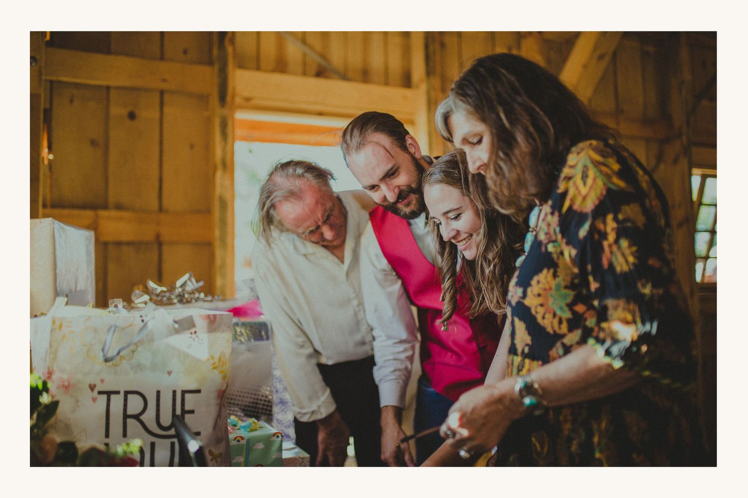 Guests gather around a rustic wedding gift table in a barn venue, smiling and opening presents together.