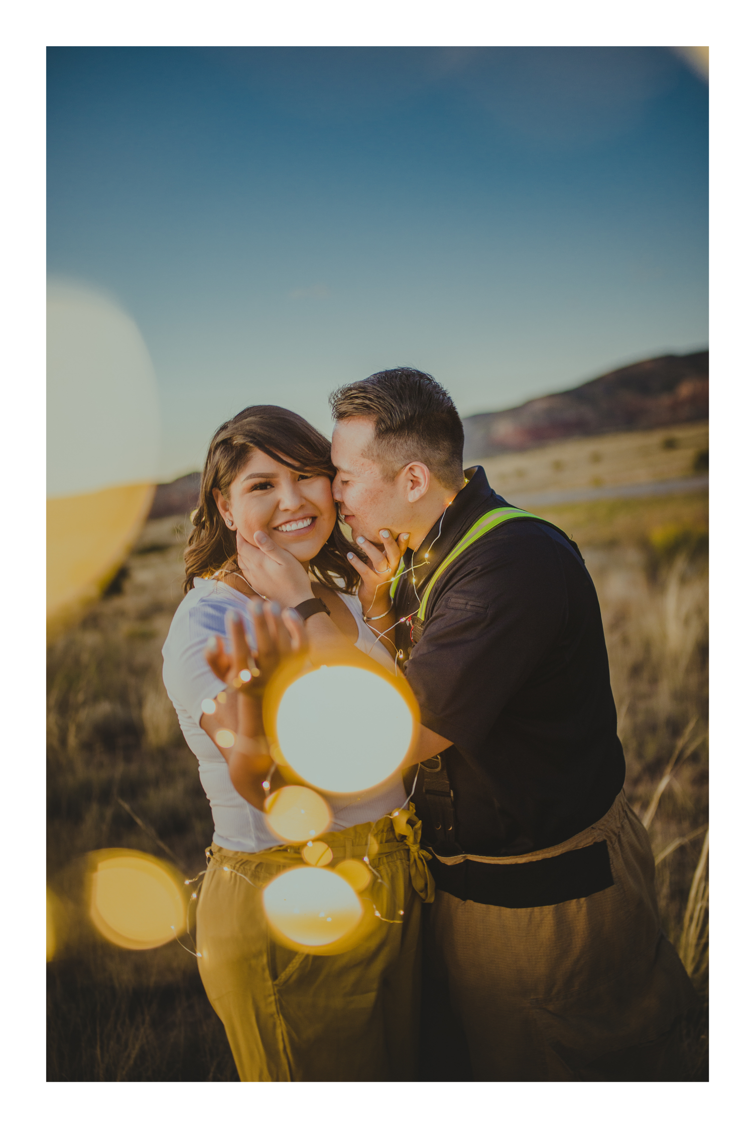 Couple sharing a romantic moment in a golden field at sunset, with beautiful lens flare bokeh effects.