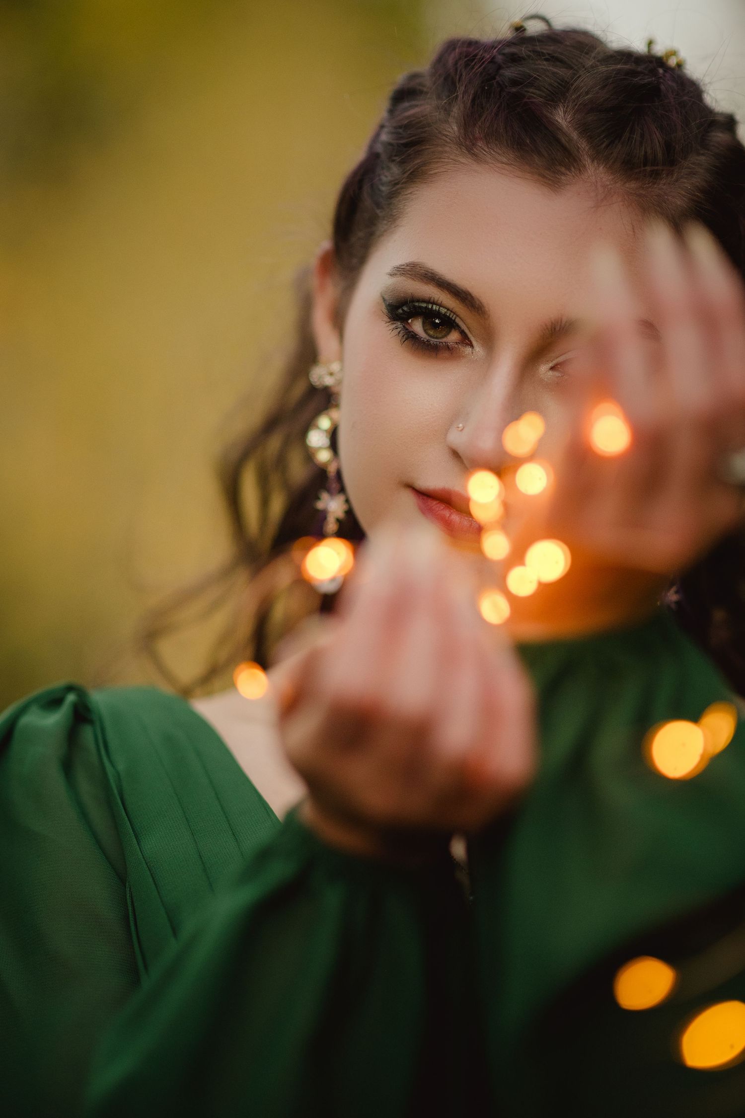 Portrait in emerald green dress with bokeh lights creating dreamy atmosphere against blurred background.