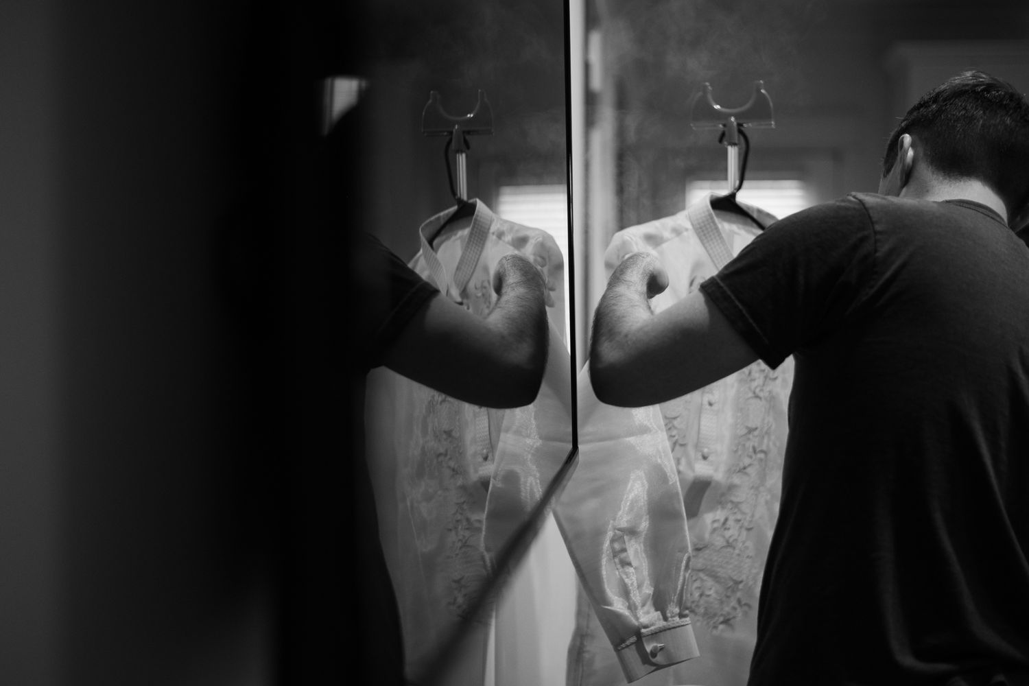 A person in a dark shirt looks into a mirror reflection creating a dramatic black and white composition.