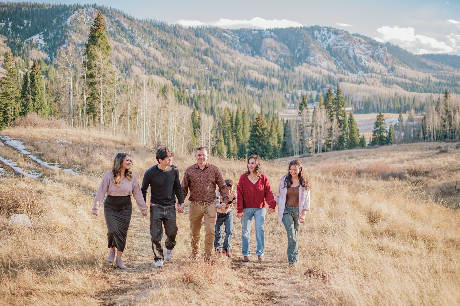A group walking along a mountain trail with scenic autumn mountains and evergreen forests in the background.