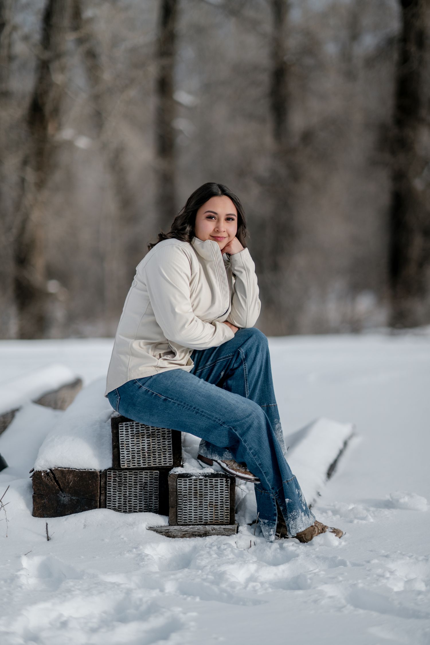 A person in a cream sweater and jeans sits on a wicker chair in a snowy winter landscape.