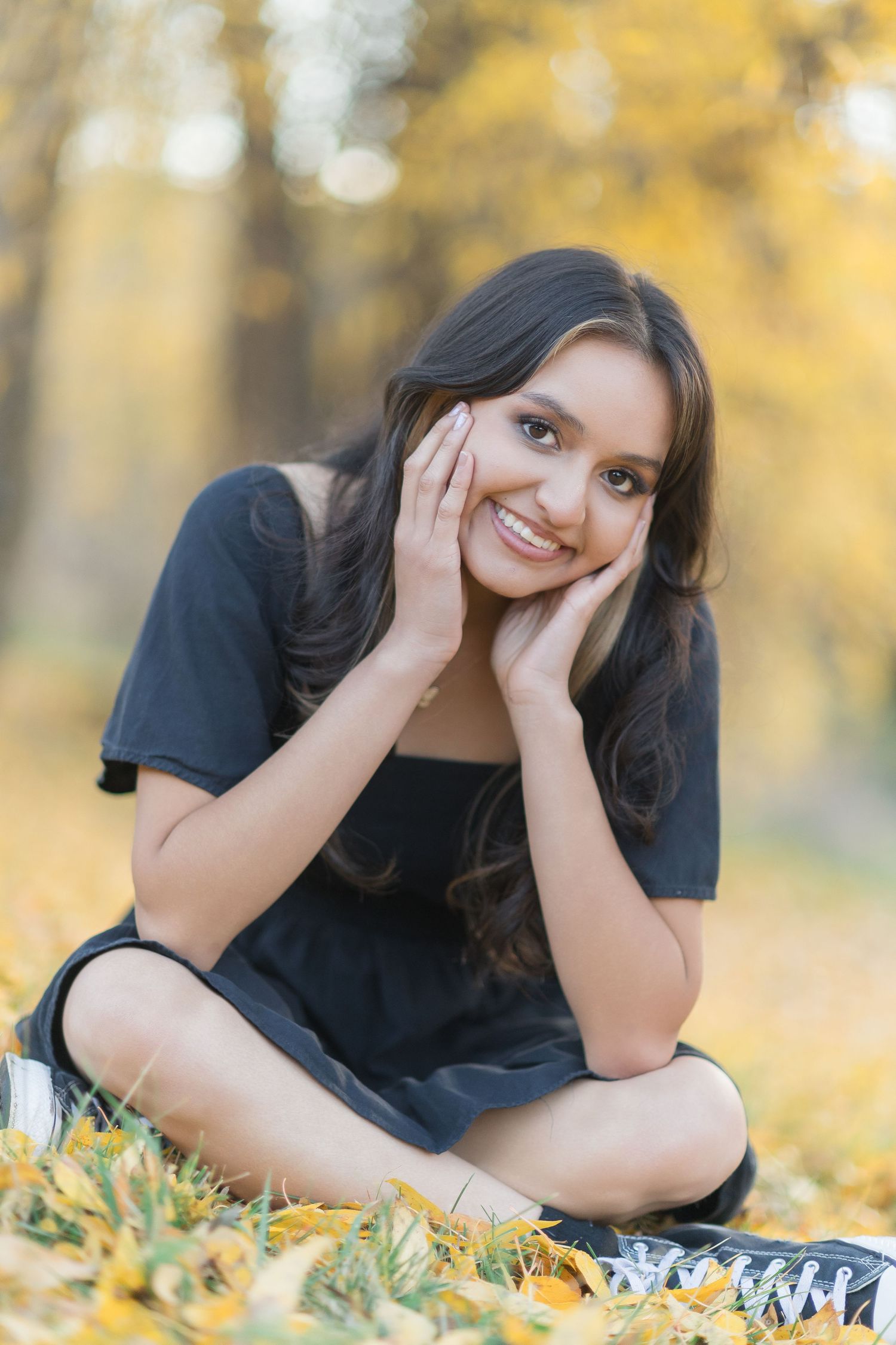 A person in a black shirt lies on autumn leaves during a golden hour photoshoot in a park.