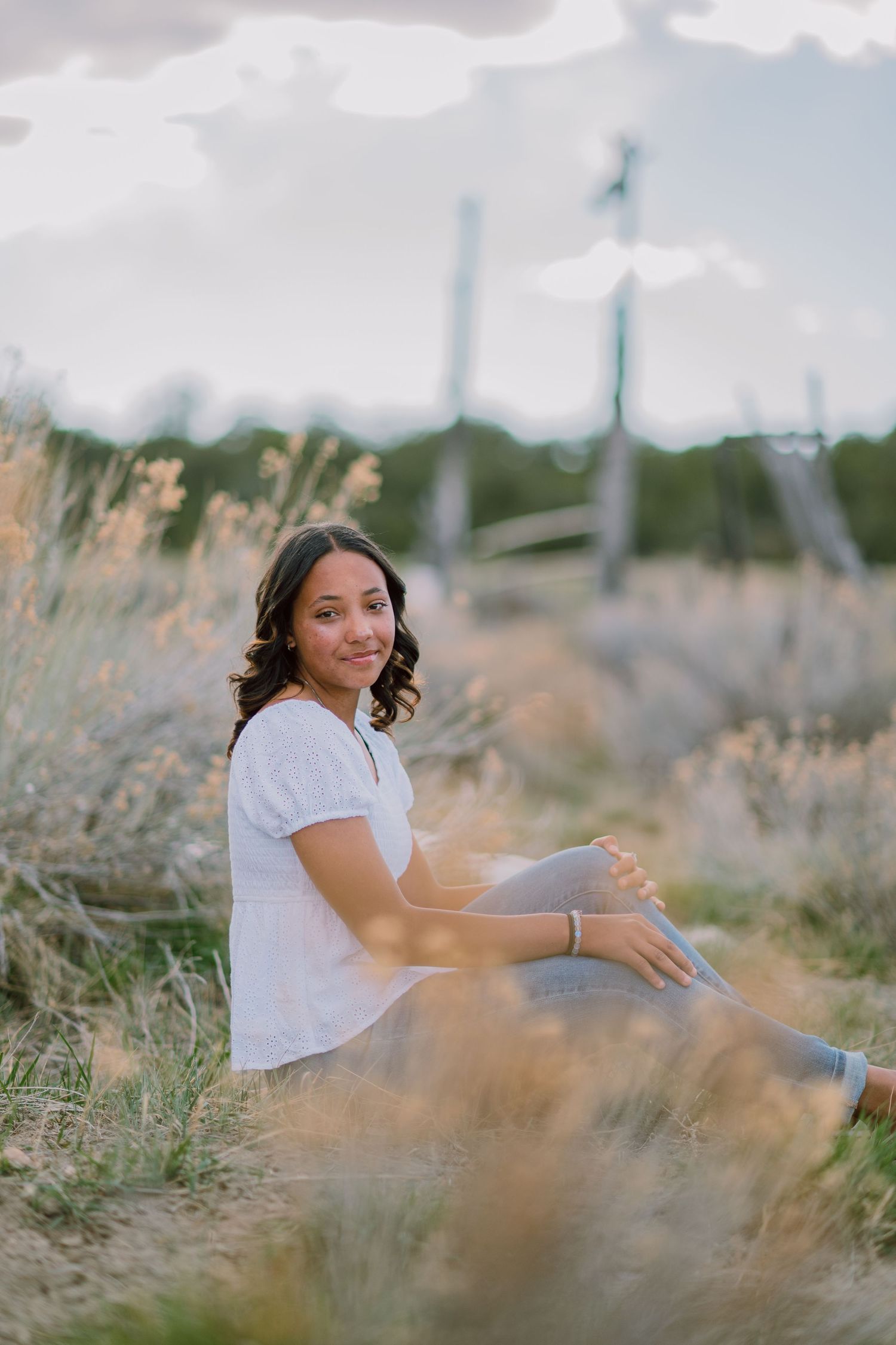 Person sitting in tall grass field during golden hour with dreamy soft focus effect.