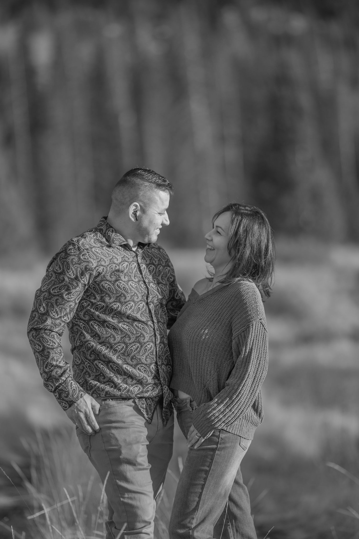 A black and white engagement photo of a couple sharing a playful moment outdoors.