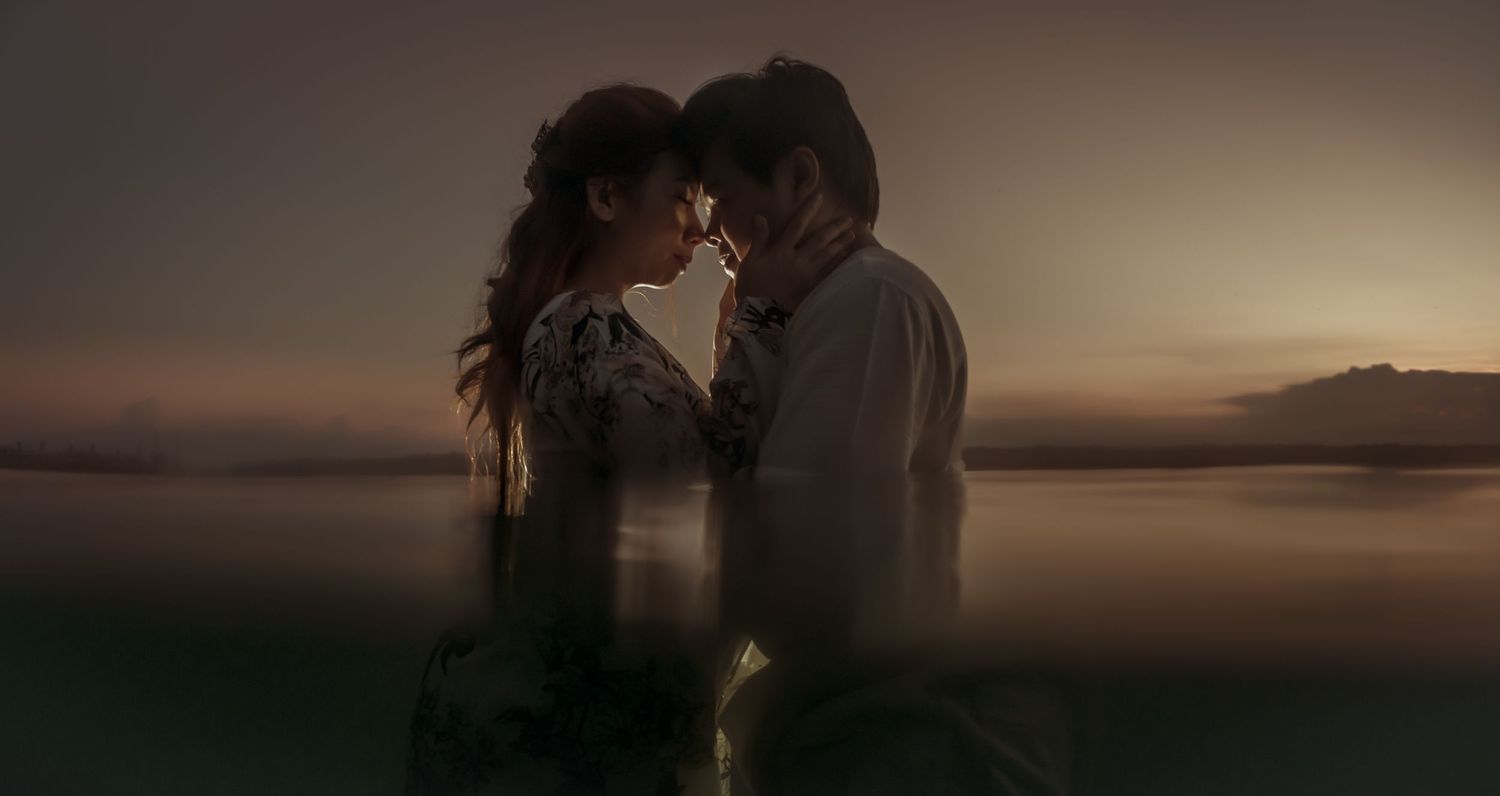 Silhouettes of a romantic moment under a wooden shelter at sunset.