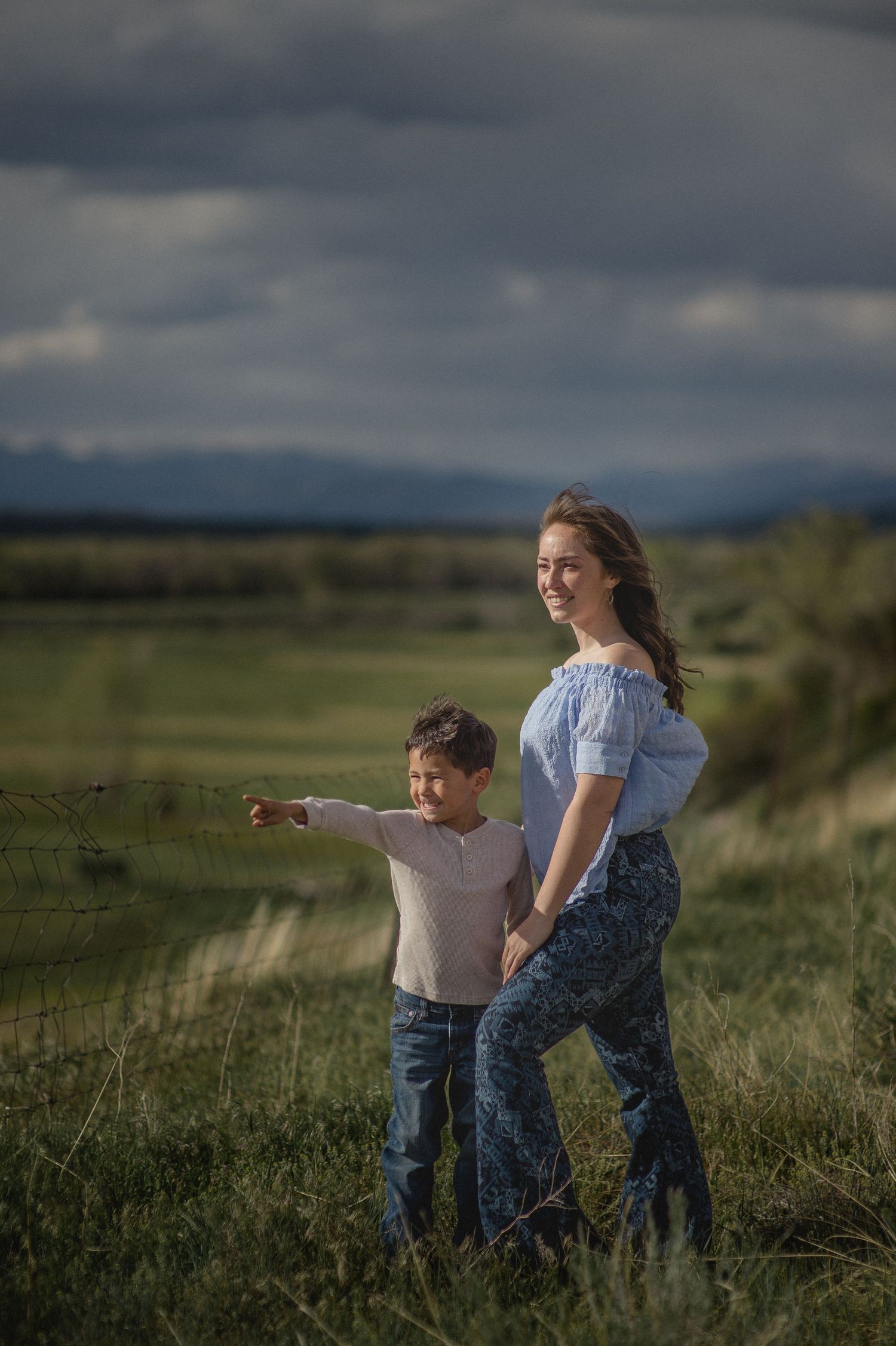 Mother and toddler son standing together in a sunlit grassy field in Los Ojos, New Mexico — tender moment by Quiet Light by The Amoras.