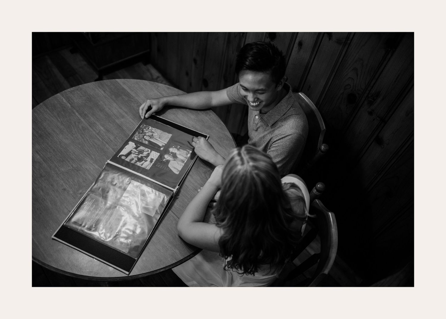 Two people looking at old photographs together at a wooden table in black and white.