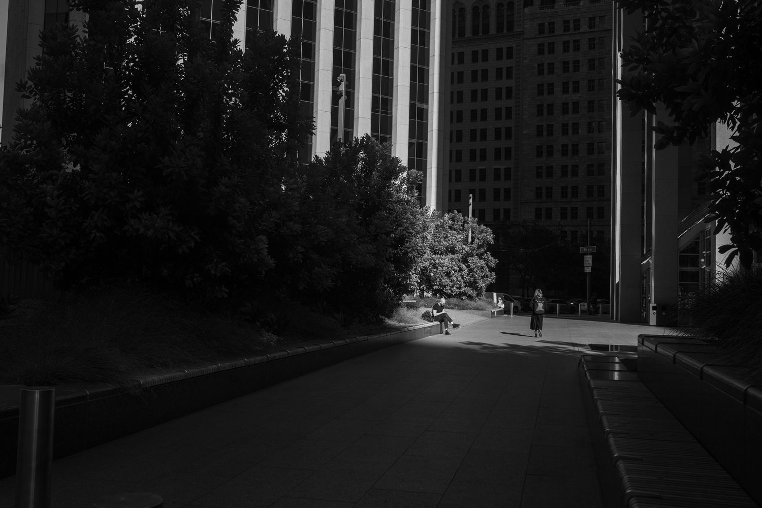 Monochrome industrial cityscape with tall buildings and poles casting shadows across an urban walkway.