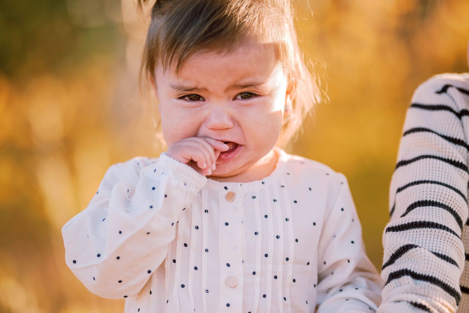A delighted young child in a polka dot shirt smiling with joy outdoors in golden sunlight.