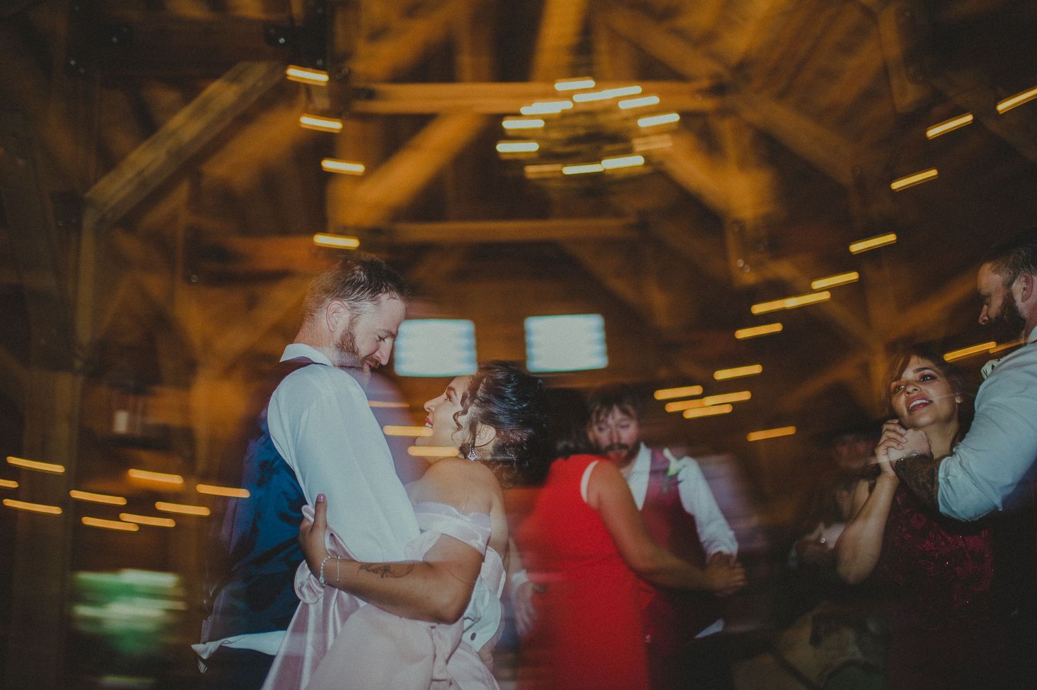 Blurred motion dance party scene in wooden barn with ambient lighting.