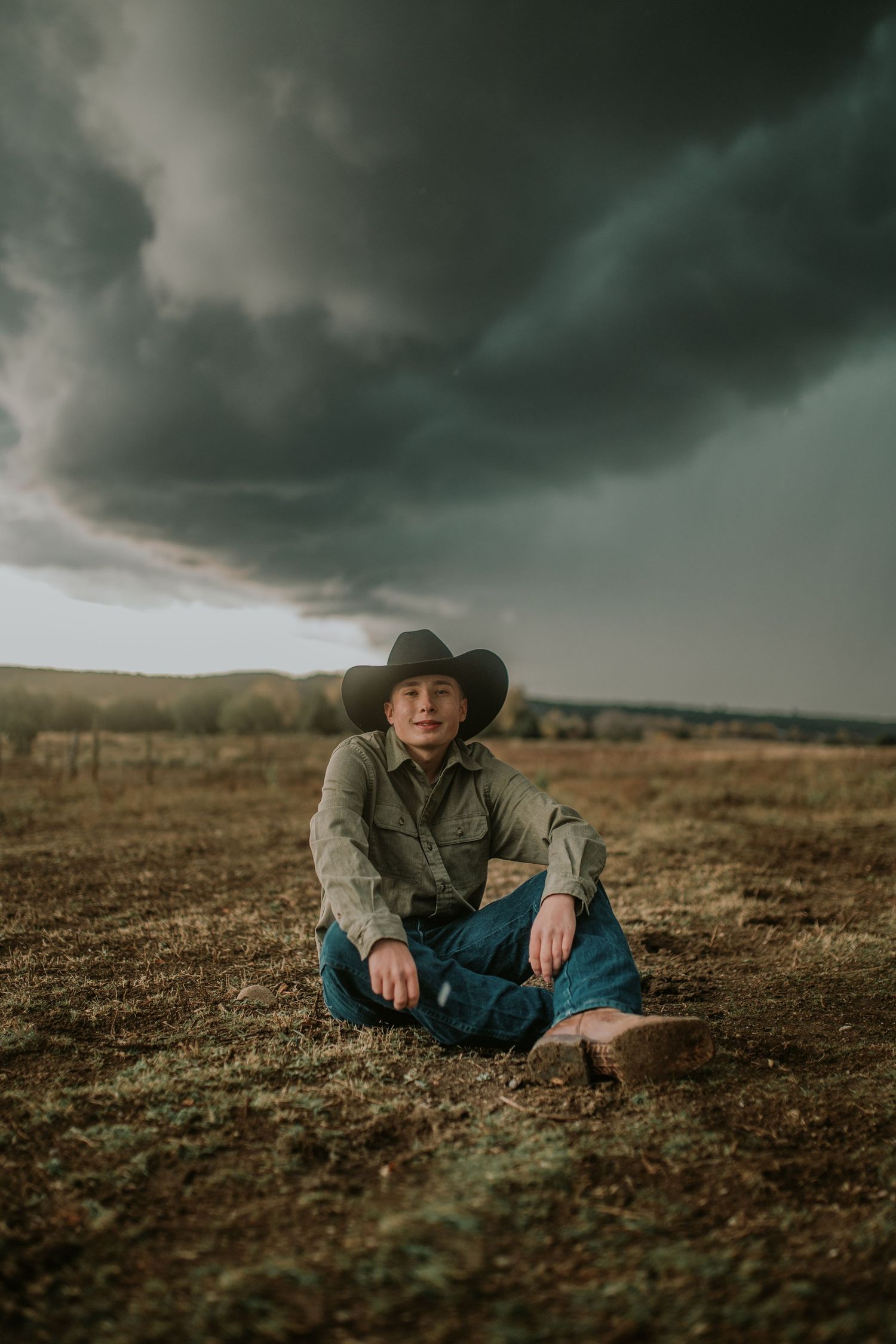 Moody series of cowboy resting on rugged terrain against dramatic stormy sky in western landscape.