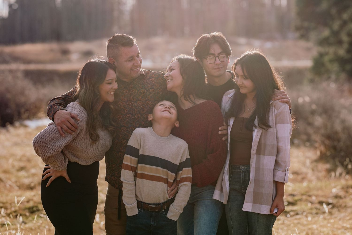 Family enjoying outdoor photo session in warm sunset light while sitting together and looking at each other lovingly.