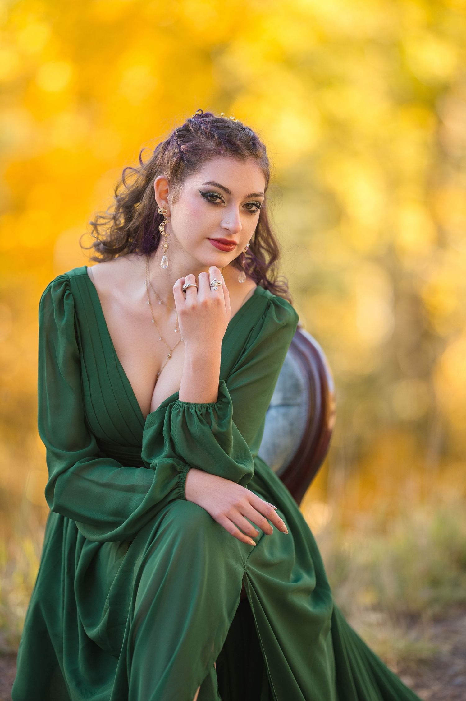 A person in an emerald green dress poses gracefully outdoors against a warm autumn background with golden bokeh.